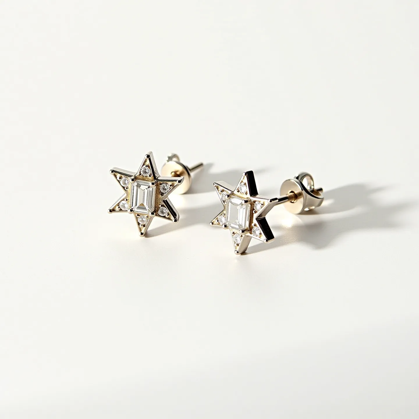 These star stud earrings feature a striking design with each earring crafted in a six-pointed star shape. The stars are adorned with a central emerald-cut gemstone, likely a diamond, which adds a touch of elegance and sophistication. Surrounding the central stone, smaller round-cut gems are meticulously set, enhancing the overall sparkle and brilliance. The earrings are made from a smooth, polished metal, possibly white gold or platinum, which complements the luminous stones. The earrings are secured with a classic post and butterfly back clasp, ensuring a secure and comfortable fit.