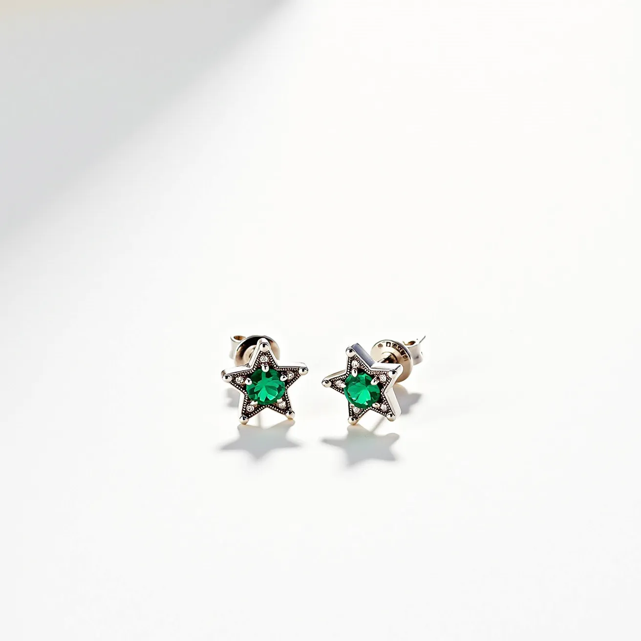 These star stud earrings feature a striking design centered around a vibrant green stone, likely an emerald or a similar gemstone, cut into a multi-faceted form that catches the light beautifully. The star-shaped outline of the earrings is crafted from a silver-toned metal, offering a sleek and modern aesthetic. Each of the five points of the star is accentuated with small round settings, possibly holding tiny clear stones or simply textured for contrast. The attachment mechanism appears to be a classic post and butterfly clasp, ensuring a secure and comfortable fit when worn.