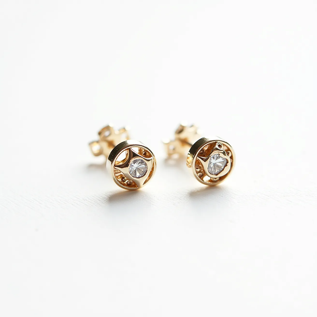 These stud earrings are crafted from gold, featuring a central round-cut gemstone that appears to be a diamond, securely held in a bezel setting. The earrings exhibit a polished finish that complements the brilliance of the gemstone. The attachment method is a classic push-back clasp, ensuring they are easy to wear and secure. The design intricately combines elegance with simplicity, highlighting the beauty of the materials used.