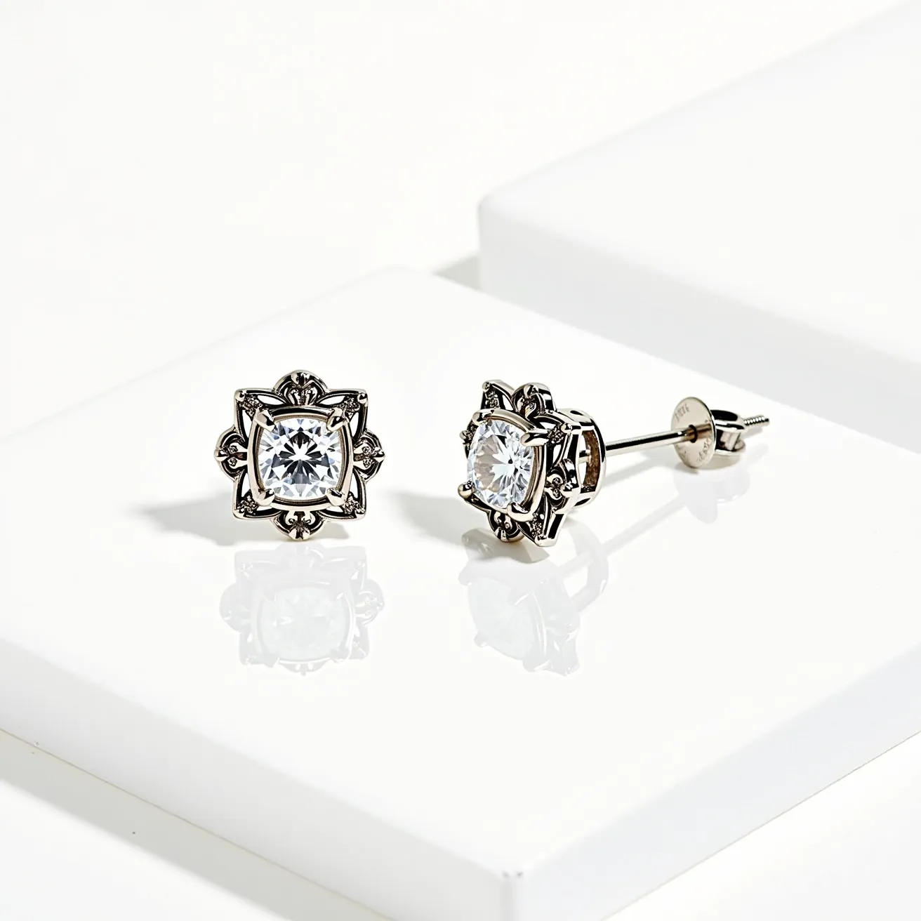 These stud earrings feature a central gemstone that appears to be a round cut, clear stone, possibly a diamond or cubic zirconia, set in a claw setting. The metal frame holding the stone is intricately designed, suggesting a detailed metallic alloy, possibly silver or white gold, with ornamental motifs. The earrings secure with a post and screw-back clasp, providing stability when worn. The overall design balances elegance and intricacy, making these studs a striking accessory.