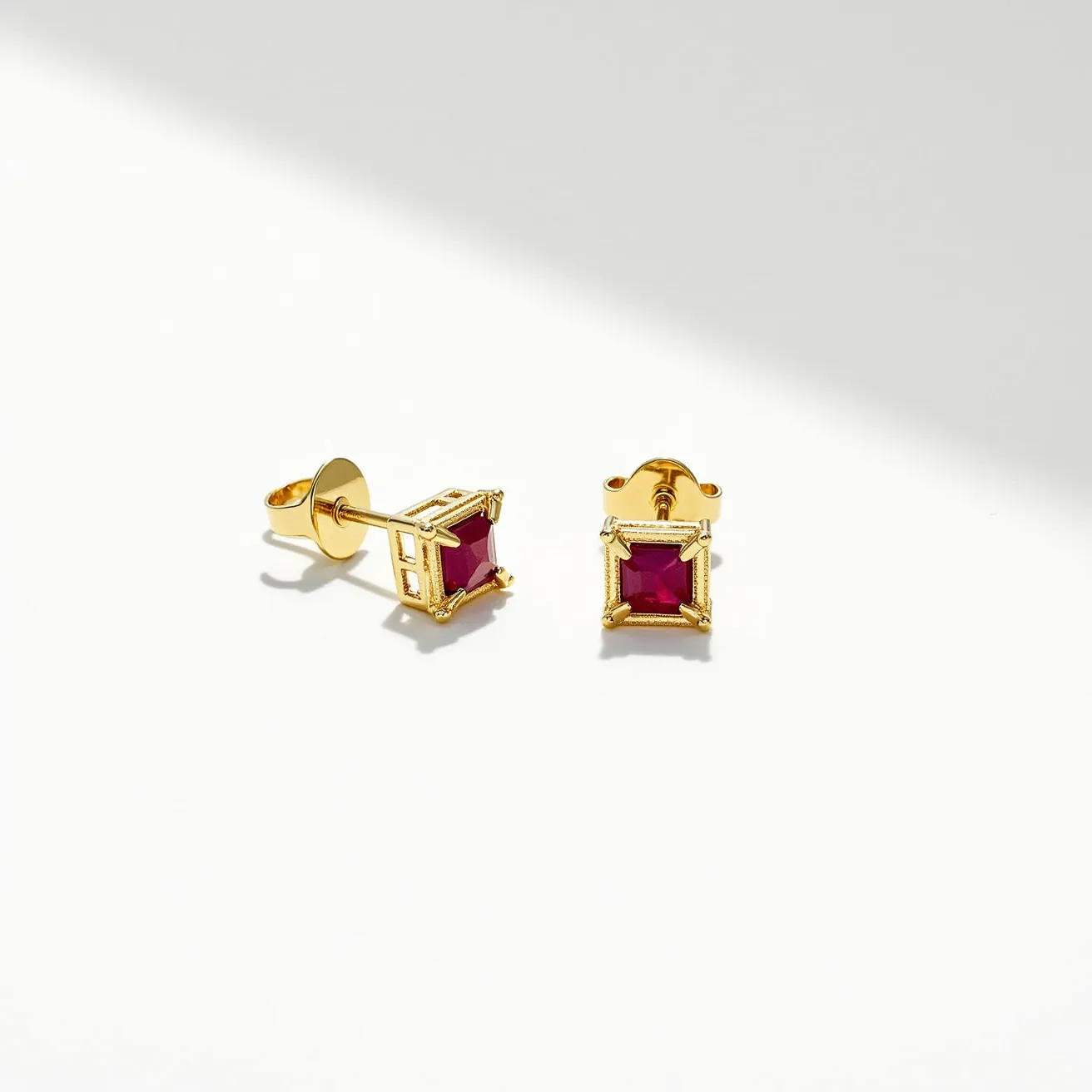 These stud earrings feature square-cut red gemstones set in a four-prong setting, likely made of a gold-colored metal that enhances their vibrant appearance. The clean lines and symmetrical design highlight the elegant characteristics of the stones, which are precisely cut to ensure maximum reflection of light. The attachment includes a classic butterfly clasp, ensuring a secure and comfortable fit on the earlobe. The overall design presents a modern yet timeless aesthetic, perfect for adding a touch of sophistication to any ensemble.