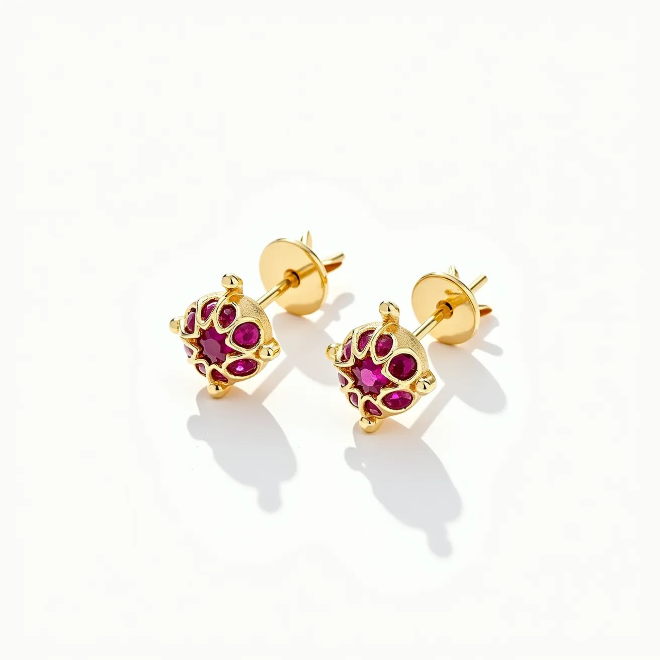 These stud earrings feature a decorative design crafted from gold-toned metal with intricate detailing. The focal point is a cluster of vibrant red gems, likely rubies, arranged in a floral or abstract pattern. Each gem appears to be round-cut and is securely set within the structure, enhancing the overall brilliance and elegance. The earrings are fitted with a classic post and butterfly clasp, ensuring secure attachment when worn. The combination of the gold finish and red gemstones creates a striking and elegant aesthetic.