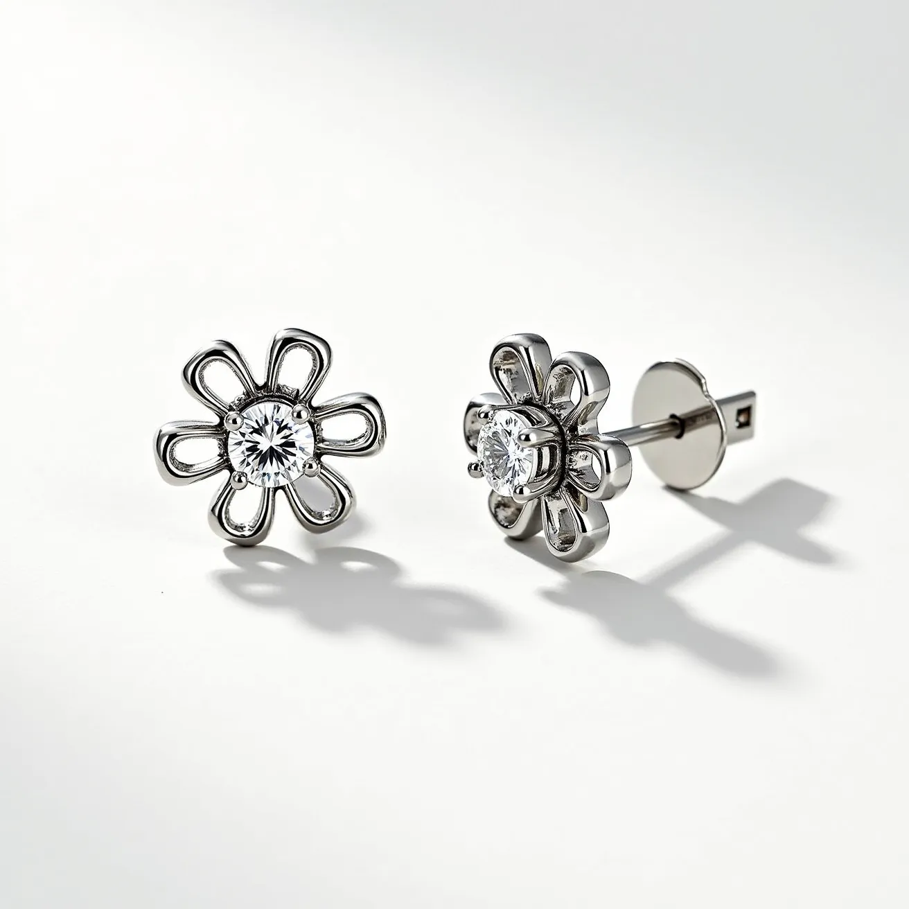 These stud earrings feature a floral design crafted from what appears to be a polished metal, likely silver or white gold, forming petal-like structures that radiate from a central gem. The centerpiece is a round-cut gemstone, possibly a diamond, set in a secure prong setting that showcases its brilliance. The earrings are attached using a straight post and a butterfly clasp, ensuring a secure and comfortable fit. The combination of the metal and the gemstone in the floral arrangement gives these earrings an elegant and classic appearance.