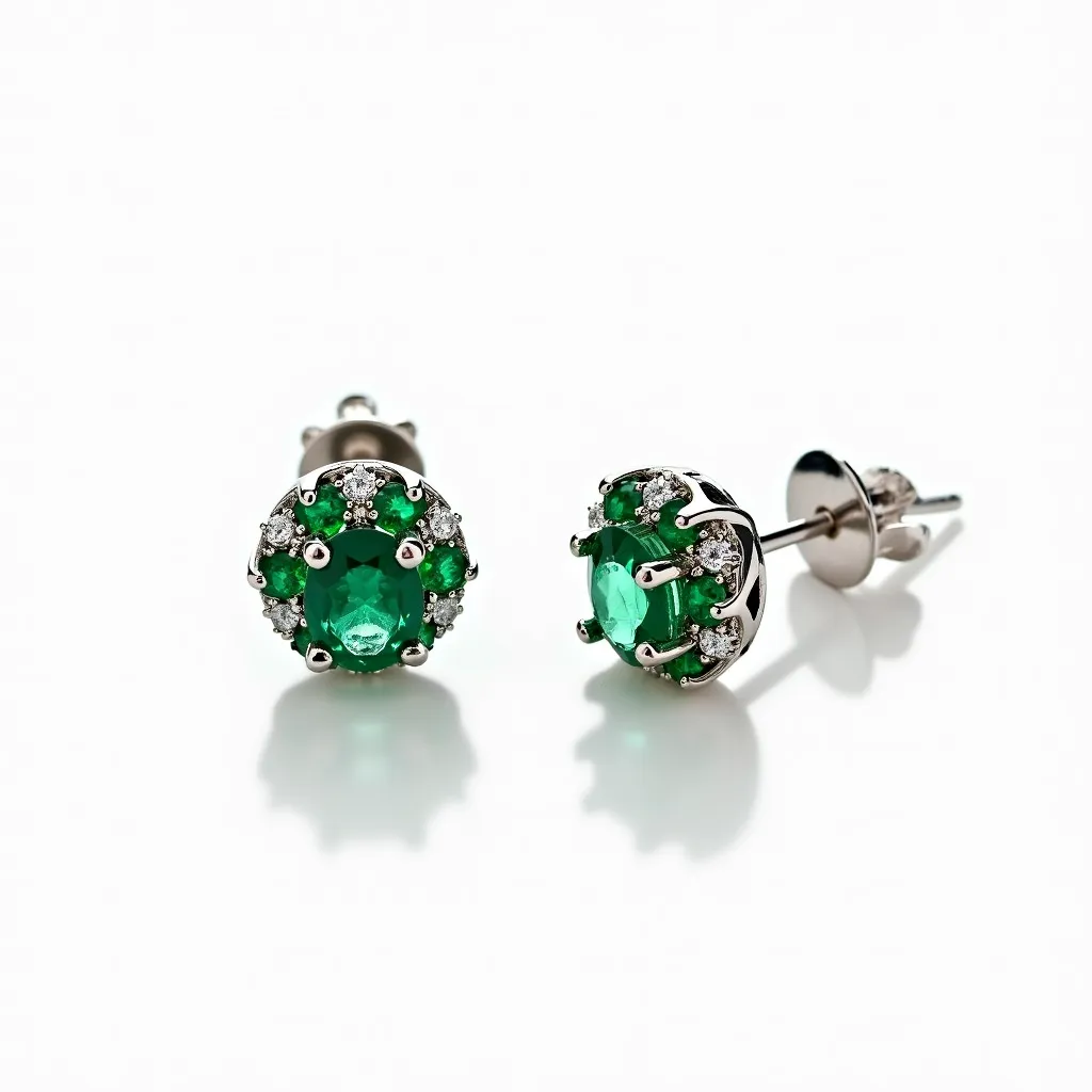 These stud earrings feature a vibrant green gemstone at the center, likely an emerald, surrounded by smaller white stones that resemble diamonds. The green gem is oval-cut and securely set with prongs, while the white stones are arranged in a halo-like formation around it. The earrings are crafted from a shiny metal, possibly white gold or platinum, which complements the brilliance of the stones. They are attached with a classic post-and-friction-back fastening, ensuring a secure and stylish fit.