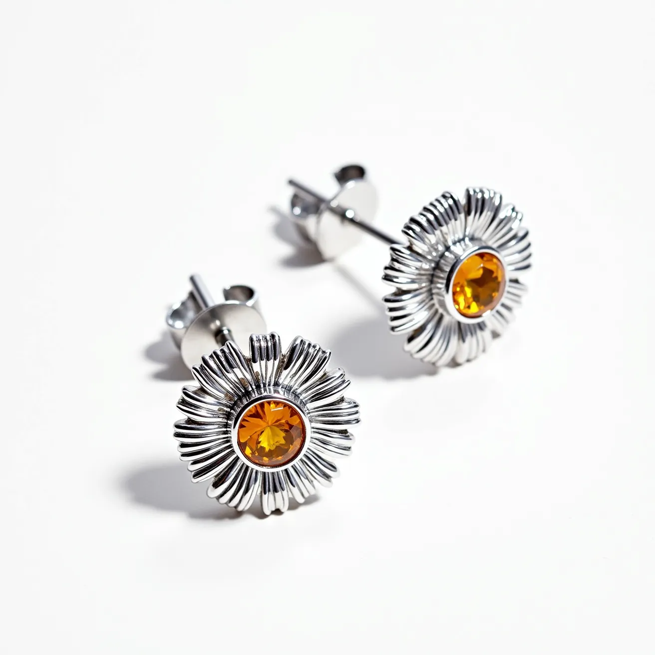 These sunflower earrings feature a radiant design with stylized petals crafted from a shiny metal, likely silver or stainless steel, surrounding a central gem. The gem appears to be a round-cut stone with a vibrant orange hue, possibly a synthetic or semi-precious stone such as citrine or topaz. This stone is set securely within a bezel setting, enhancing its vibrant color and reflecting light beautifully. The earrings are equipped with a post and butterfly clutch fastening, ensuring they are secured comfortably to the ear. This combination of materials and design elements makes these earrings both striking and elegant.