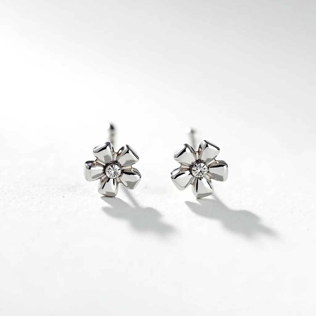 These teacher earrings feature a delicate flower design, likely crafted from a polished silver or white gold material, giving them a sleek and shiny appearance. At the center of each flower is a small round gem, possibly a diamond or a similarly cut stone, securely set to enhance the overall sparkle of the earrings. The petals are elegantly curved, adding a three-dimensional aspect to the design. These earrings are equipped with a standard post backing, which is a common and secure fastening method for stud earrings.