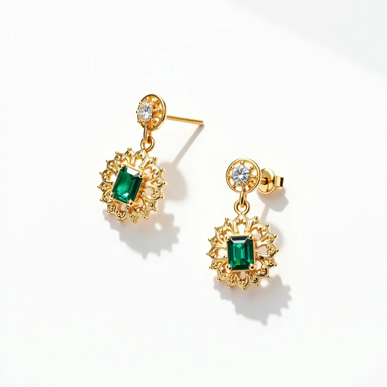 These teacher earrings feature a sophisticated design with a gold-toned setting. At the top of each earring is a round-cut clear gemstone set in a simple bezel setting, creating an elegant stud. Suspended from this, the lower drop element showcases a vibrant, emerald-cut green gemstone surrounded by an intricate gold filigree halo. The earrings are secured with a classic post-and-screw back clasp, ensuring a secure fit and comfortable wear. The overall combination of green and clear stones with the gold detailing creates a refined and stylish look.