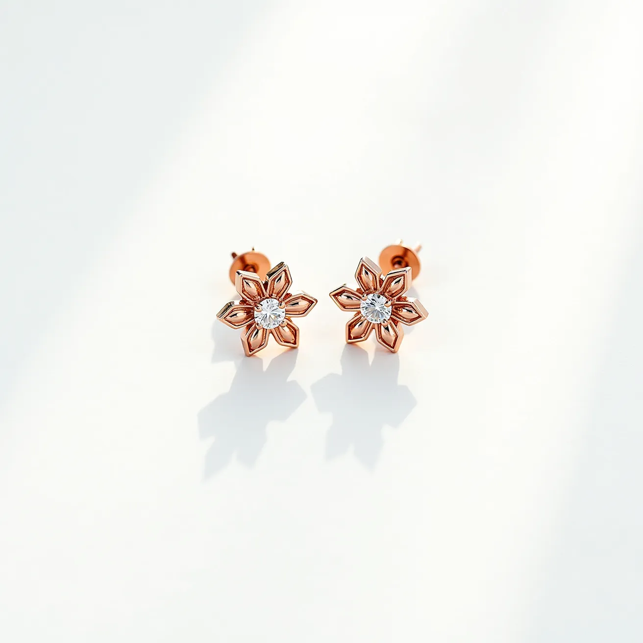 These teacher earrings are designed in the shape of flowers with rose gold petals, each intricately crafted to form a six-petal motif. At the center of each earring is a round, clear gemstone, likely a diamond or cubic zirconia, which has been cut with precision to enhance its sparkle and set in a prong setting that securely holds the stone in place. The earrings feature a post-back clasp, ensuring they remain comfortably and securely attached when worn. The combination of the warm rose gold and the brilliant central stone creates a striking and elegant appearance, suitable for both everyday wear and special occasions.