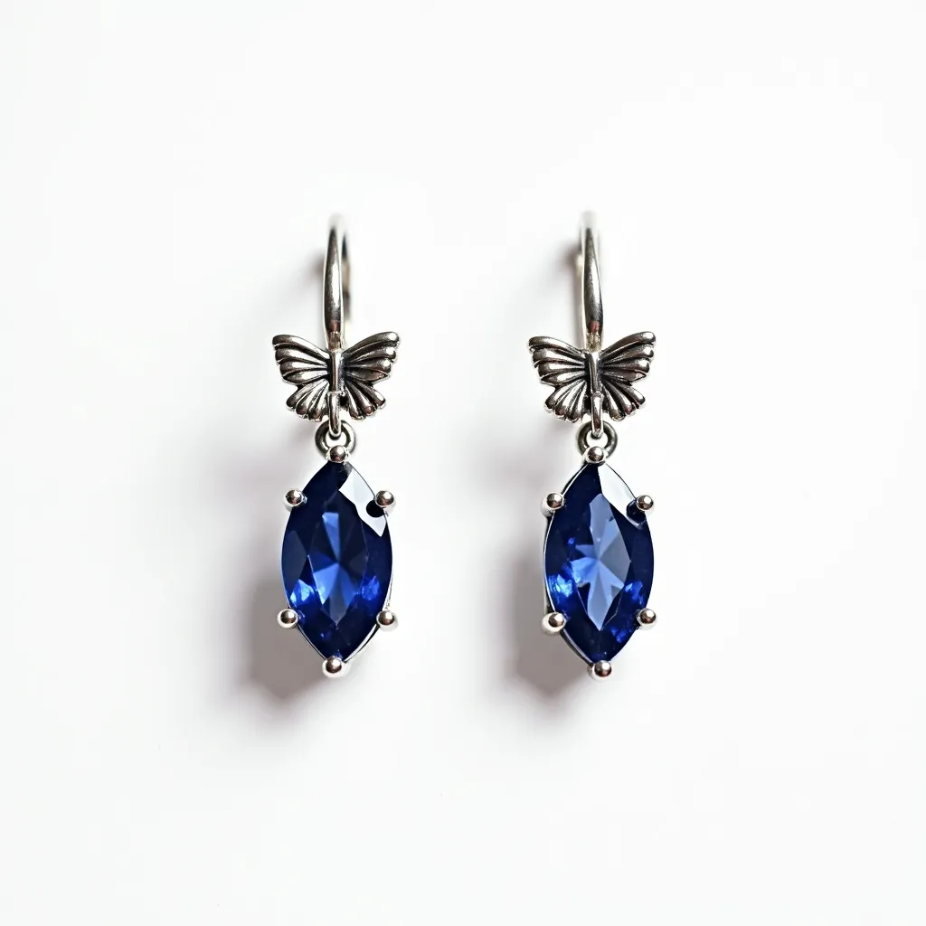 These teacher earrings feature an elegant design with a prominent deep blue marquise-cut stone, securely held by prong settings. The earrings are crafted with a metallic finish, likely silver, giving them a sophisticated and polished appearance. At the top, a delicate butterfly motif adds a whimsical touch, connecting the stone to the earring hook, which serves as the attachment mechanism. The combination of the blue stone and the silver metal creates a striking contrast, making these earrings both eye-catching and stylish.