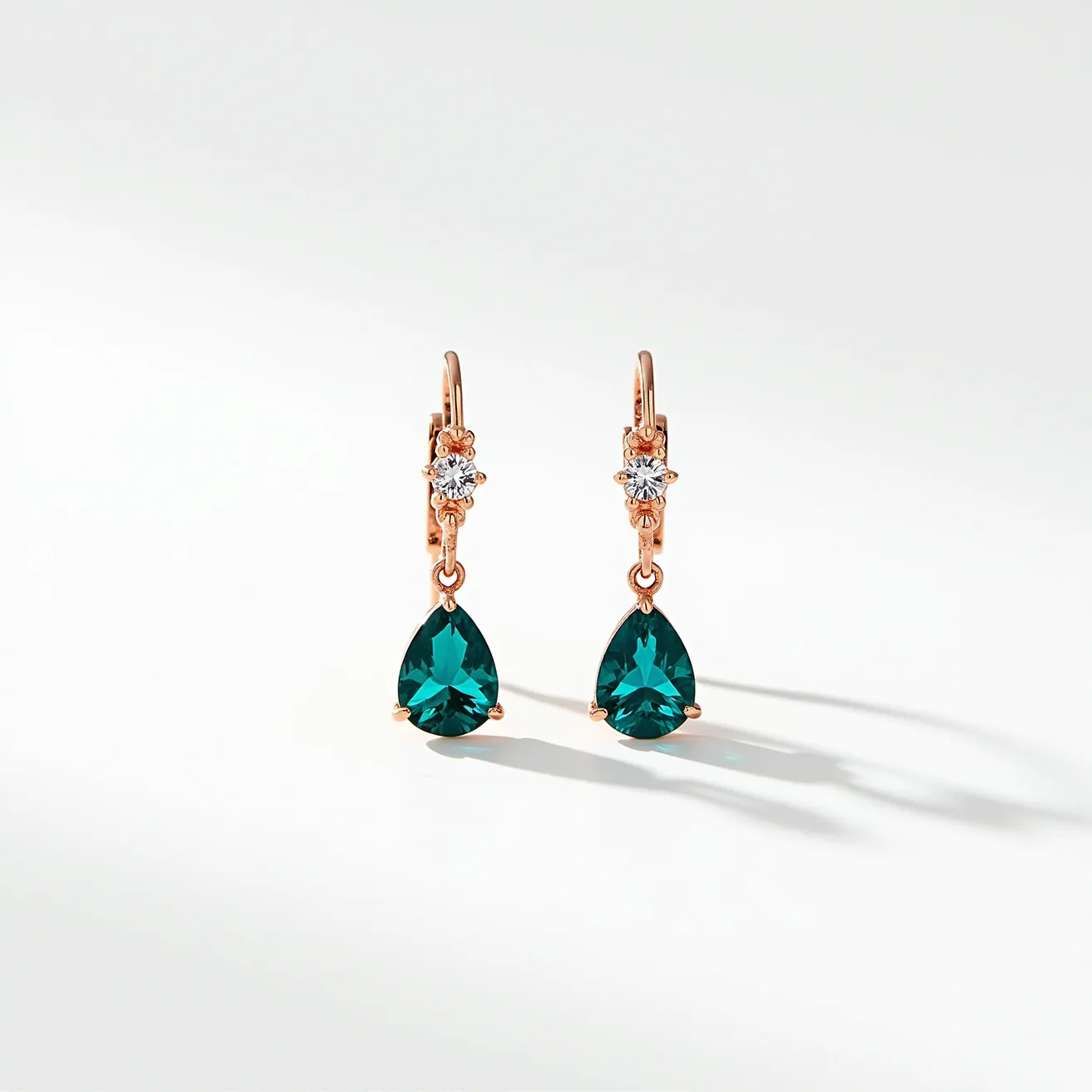 These teal earrings feature a striking teardrop-shaped gemstone that is elegantly cut to enhance its vibrant teal hue. The gemstone is set in a delicate prong setting, which allows for maximum light entry, enhancing the stone's natural brilliance. Above the teal teardrop, a smaller, round white gemstone is similarly set, providing a sophisticated contrast and adding to the earrings' allure. The earrings are attached to a rose gold lever-back clasp, which ensures secure wear while adding a touch of warmth and elegance to the overall design. The combination of colors and materials results in a versatile and stylish accessory that captures attention.