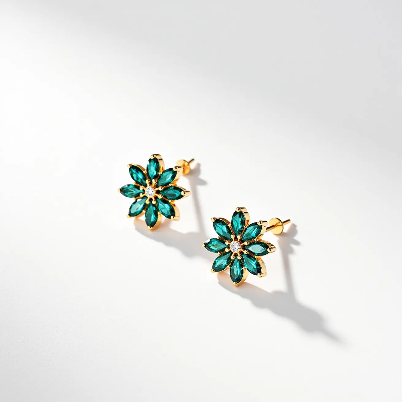 These teal earrings feature a floral design crafted with marquise-cut teal gems, artfully arranged to mimic the petals of a flower. Each petal is securely set in a golden metal base, providing a beautiful contrast and enhancing the vibrancy of the stones. The center of the floral design is adorned with a small round gem, possibly a white or clear stone, that adds a touch of sparkle and elegance. The earrings utilize a post-and-clutch fastening, offering a secure and comfortable fit, making them suitable for various occasions while maintaining a stylish and refined appearance.