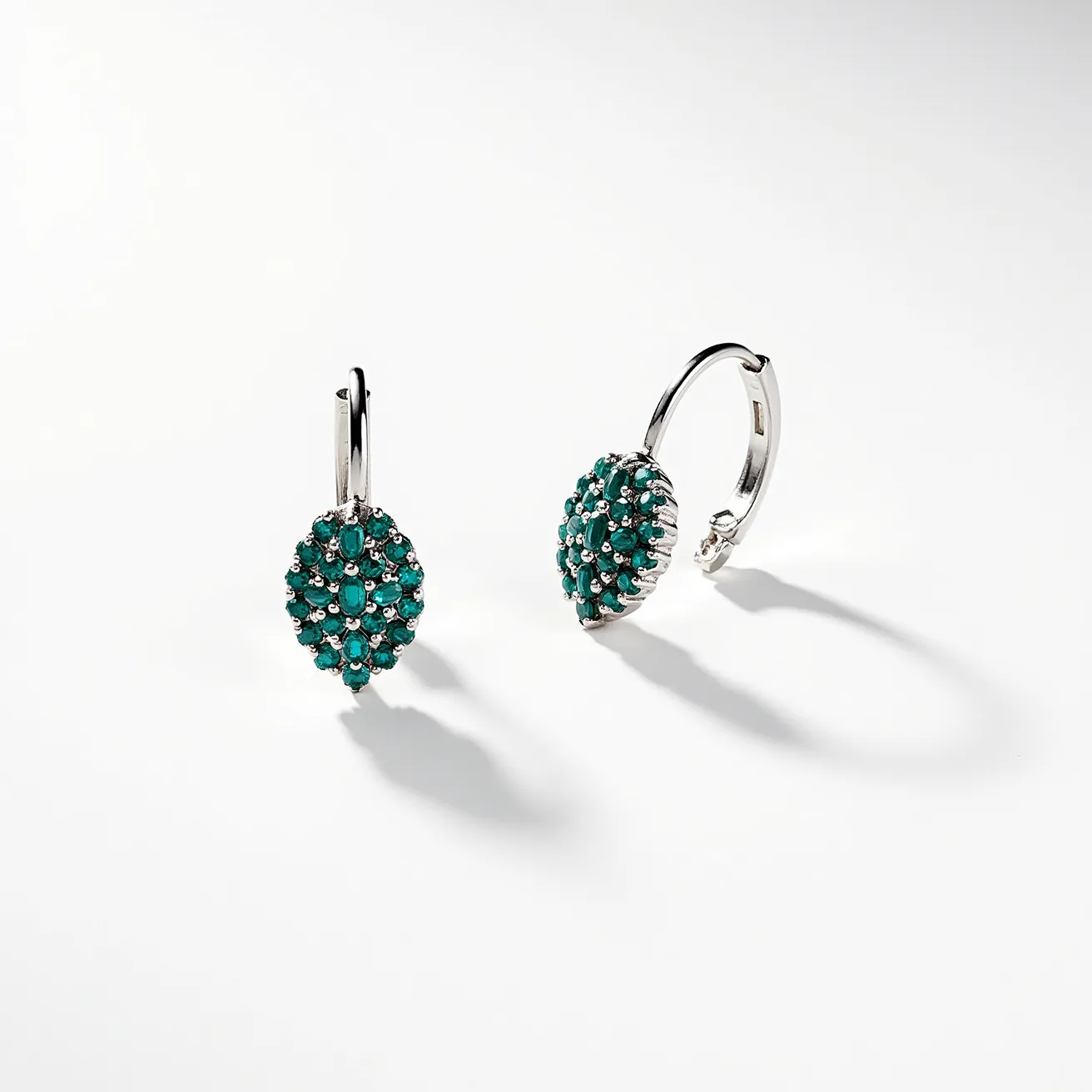 These teal earrings feature a sophisticated design, prominently showcasing a cluster of small, round opaque teal stones, possibly set in a pavé style, creating an enticing leaf shape. The stones are securely set in a bright metal, likely silver or white gold, enhancing their vibrant hue. The earrings are hoop-style, with a secure latch back closure, ensuring comfort and stability when worn. The meticulous arrangement of the stones and the elegant metal work highlight the craftsmanship involved in their creation.