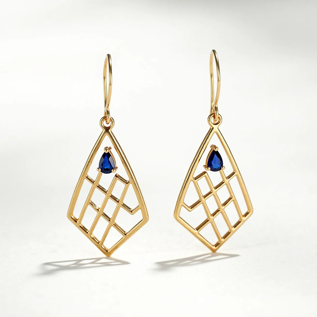 These teardrop earrings feature an open latticework design crafted from gold-toned metal, offering a modern and elegant appearance. Each earring is adorned with a small, teardrop-shaped blue gemstone, likely a sapphire, set securely at the top of the teardrop frame, which provides a rich contrast to the gold. The gemstones are held in place by three prongs that accentuate their shape and brilliance. The earrings are attached via a simple yet effective hook clasp, ensuring ease of wear while maintaining a secure fit.