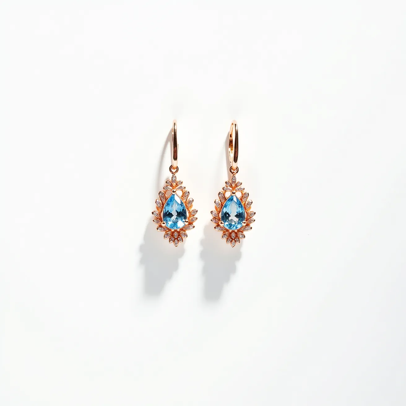 These teardrop earrings are crafted with a polished metal, likely gold, forming an intricate design that holds a prominent teardrop-shaped blue gemstone at the center. The gemstone is cut with precision to enhance its brilliance and is surrounded by a detailed halo of smaller, clear stones that accentuate its shape. The setting features a mix of prong and pave techniques, ensuring the stones are secure while maximizing their sparkle. The earrings are attached with lever-back clasps, providing both security and comfort for wearing.