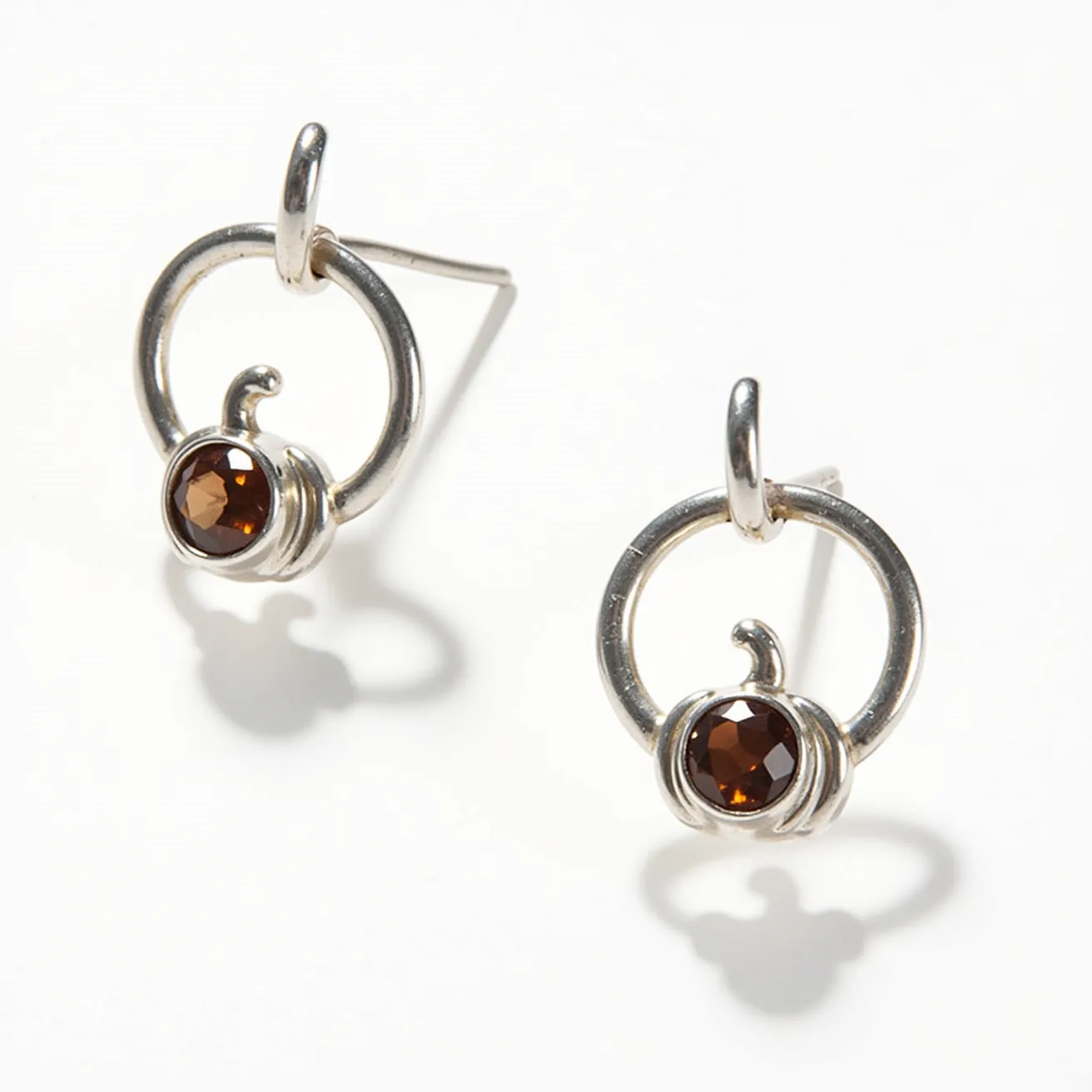 These Thanksgiving earrings feature a charming circular design crafted from polished metal, likely silver. Each earring showcases a round, faceted brown gemstone, which serves as the centerpiece. The stones are held securely in place with a bezel setting, enhancing their rich, warm color. The earrings offer a simple, yet elegant, design that captures the essence of the Thanksgiving season. The attachment features a straightforward post, indicating these are stud earrings, making them easy to wear and suitable for various occasions.