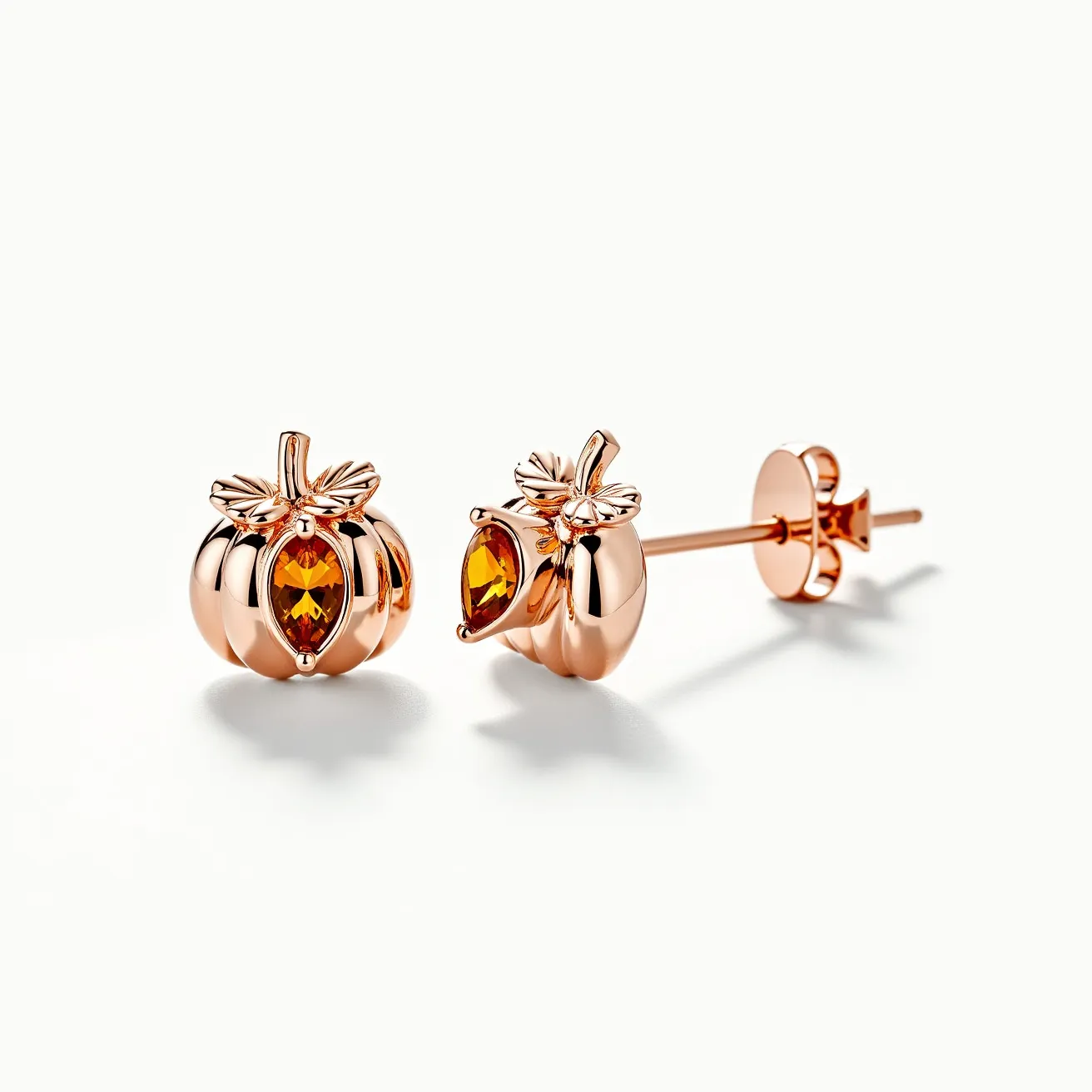 These Thanksgiving earrings are crafted in a rose gold-tone metal, skillfully shaped like pumpkins, with detailed leaf and stem accents enhancing their festive theme. Each earring features a marquise-cut orange gemstone securely set at the center, reflecting the autumnal color palette often associated with Thanksgiving celebrations. The cut of the gem is designed to catch the light, adding a subtle shimmer to the earrings. The attachment is a classic post-back, offering secure and comfortable wear for pierced ears.