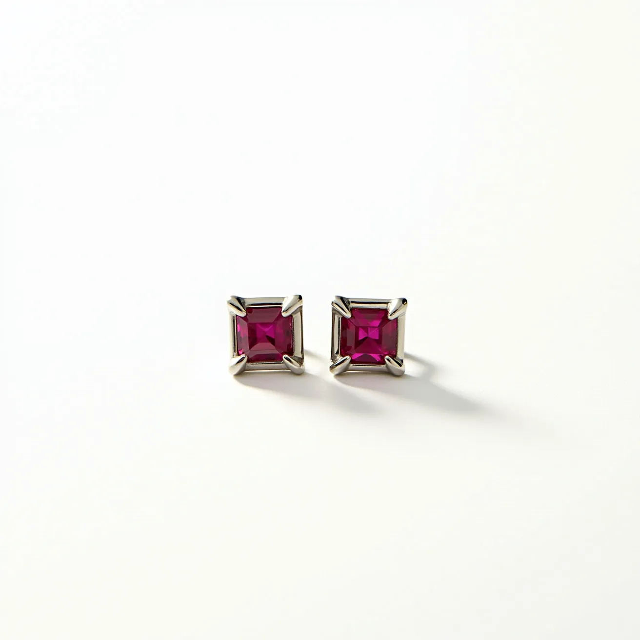 These titanium earrings feature a striking design with square-cut gems that are a deep pink, possibly rubies or garnets, set in a secure four-prong setting. The gems are meticulously cut to enhance their brilliance, catching light beautifully from every angle. The titanium setting provides durability and a modern touch, complementing the vibrant stones. The earrings are likely equipped with a push-back closure, ensuring ease of wear and stability. The overall design showcases a blend of contemporary elegance and functionality, making them a versatile accessory.