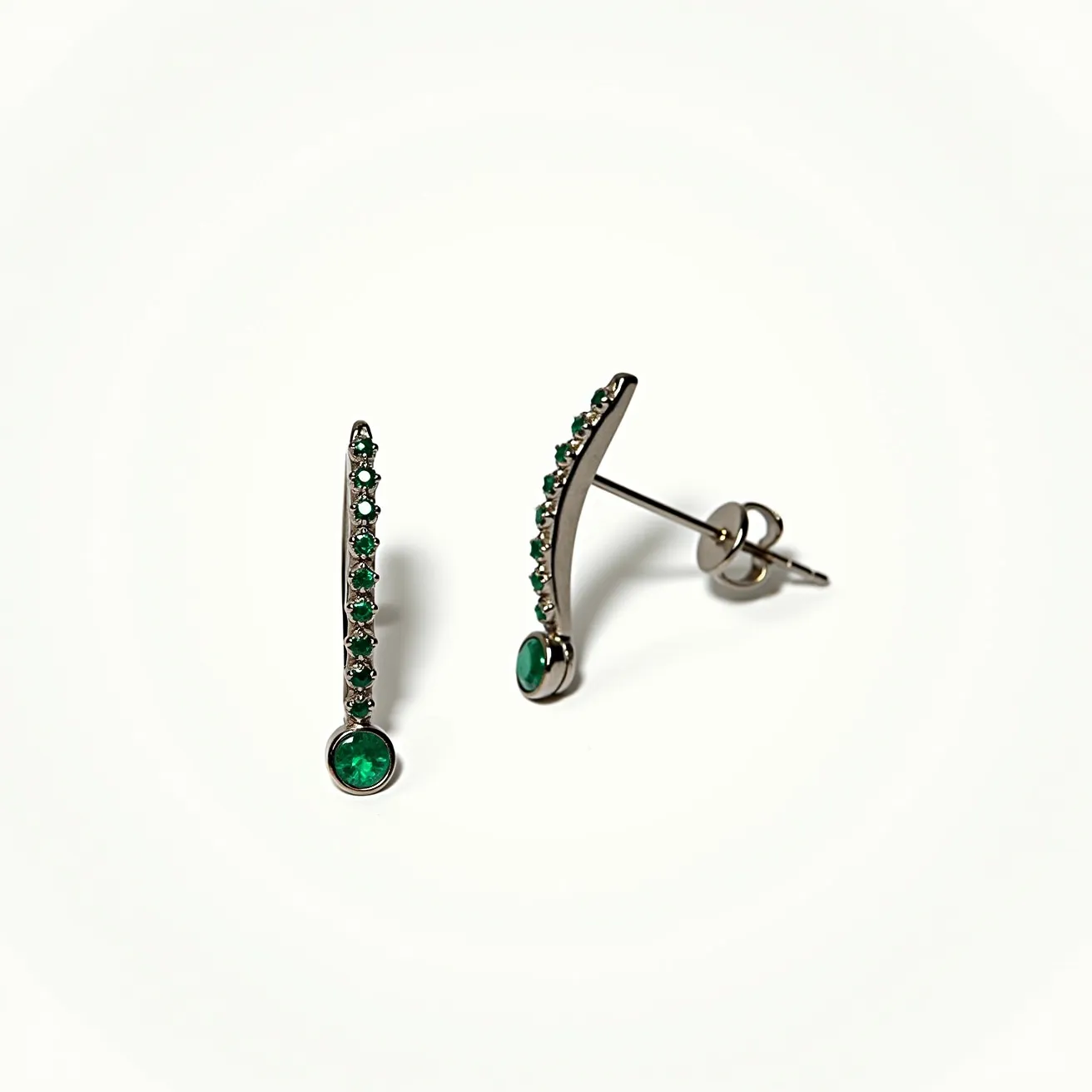 These titanium earrings feature a sleek, curved design adorned with small, round-cut green gems set in a row along the metal's surface. At the end of each earring is a larger, prominent round green gem, set in a bezel setting for secure placement. The earrings attach with a post and butterfly clasp, ensuring they stay in place when worn. The choice of titanium provides a modern and durable frame for the vibrant green stones, enhancing both aesthetics and resilience.