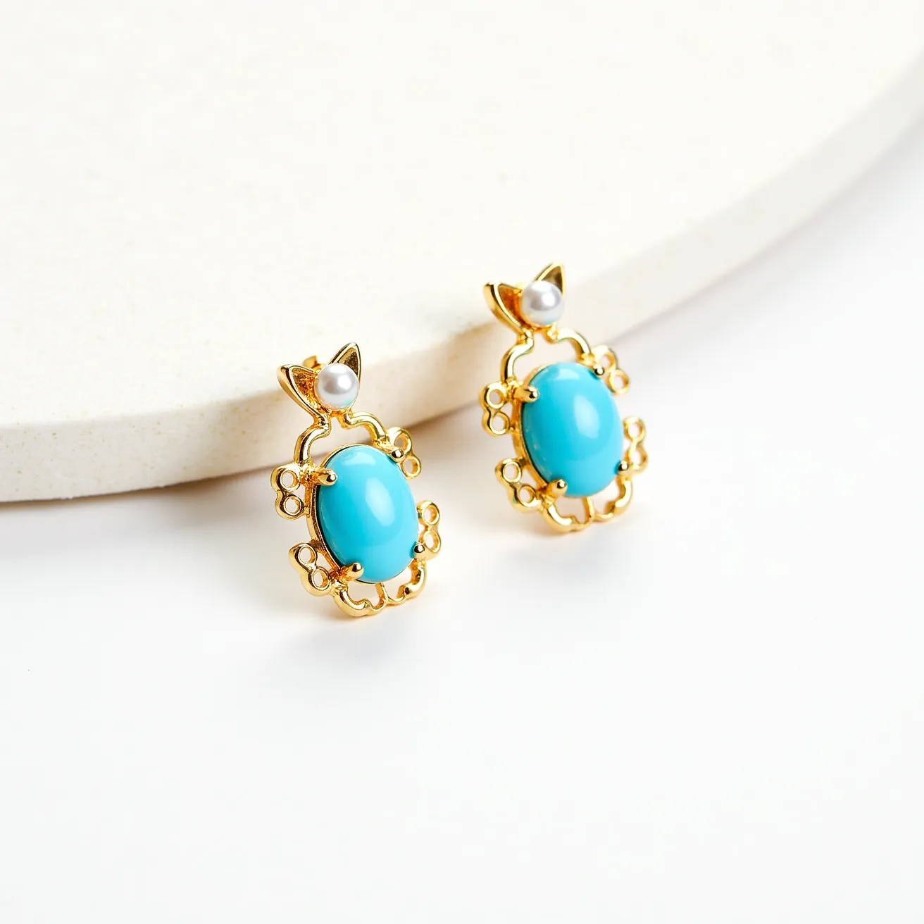 These turquoise stud earrings feature a prominent turquoise gemstone in an elegant oval cabochon cut, set within a decorative gold-toned metal frame. The frame exhibits a delicate, ornate design that encircles the stone, adding a touch of sophistication. At the top of each earring is a small, lustrous pearl-like bead acting as an accent, creating a balanced and graceful appearance. The earrings are designed with a post back, ensuring a secure fit for the wearer. The combination of turquoise, gold-toned metal, and the pearl-like bead results in a refined and stylish accessory.