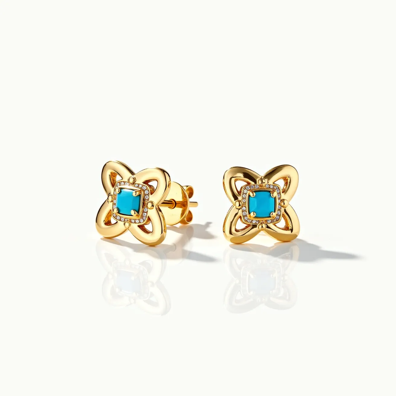 These turquoise stud earrings feature a vibrant square-cut turquoise stone at the center, surrounded by a halo of small round clear gems, likely diamonds, enhancing their brilliance. The stones are set in a gold-toned metal, which forms a decorative floral or quatrefoil motif around the centerpiece, adding an elegant and intricate design. The earrings utilize a post-back clasp, providing a secure and comfortable fit for the wearer. The combination of turquoise and gold creates a striking contrast, making these earrings a standout accessory with a sophisticated flair.