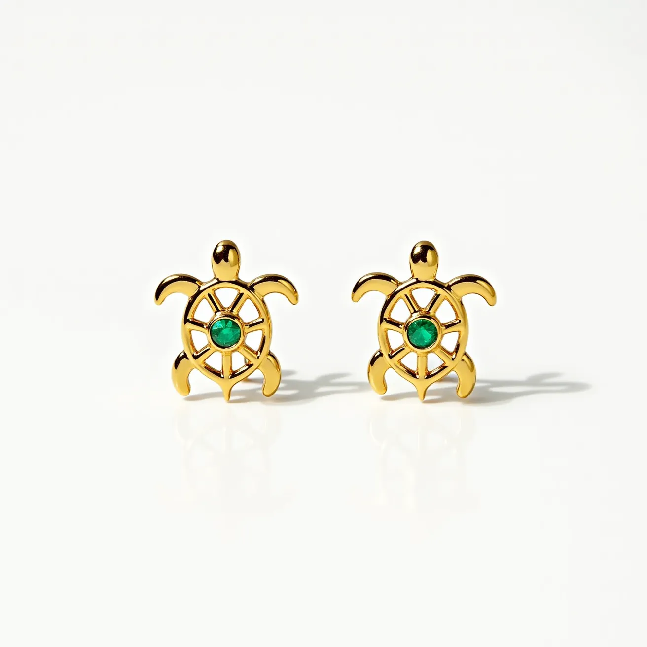 These turtle earrings feature a design where each turtle is crafted from gold-tone metal. The body of each turtle incorporates an openwork pattern resembling a turtle shell, with a small, round green stone set at the center, which could be an emerald or a similar gemstone. The stone is held with a bezel setting, ensuring it is securely placed within the shell design. The earrings attach with posts, likely including push or screw backs for securing them to pierced ears. The craftsmanship highlights the detailed representation of turtles, balanced by the elegant simplicity of the green stones in the center.