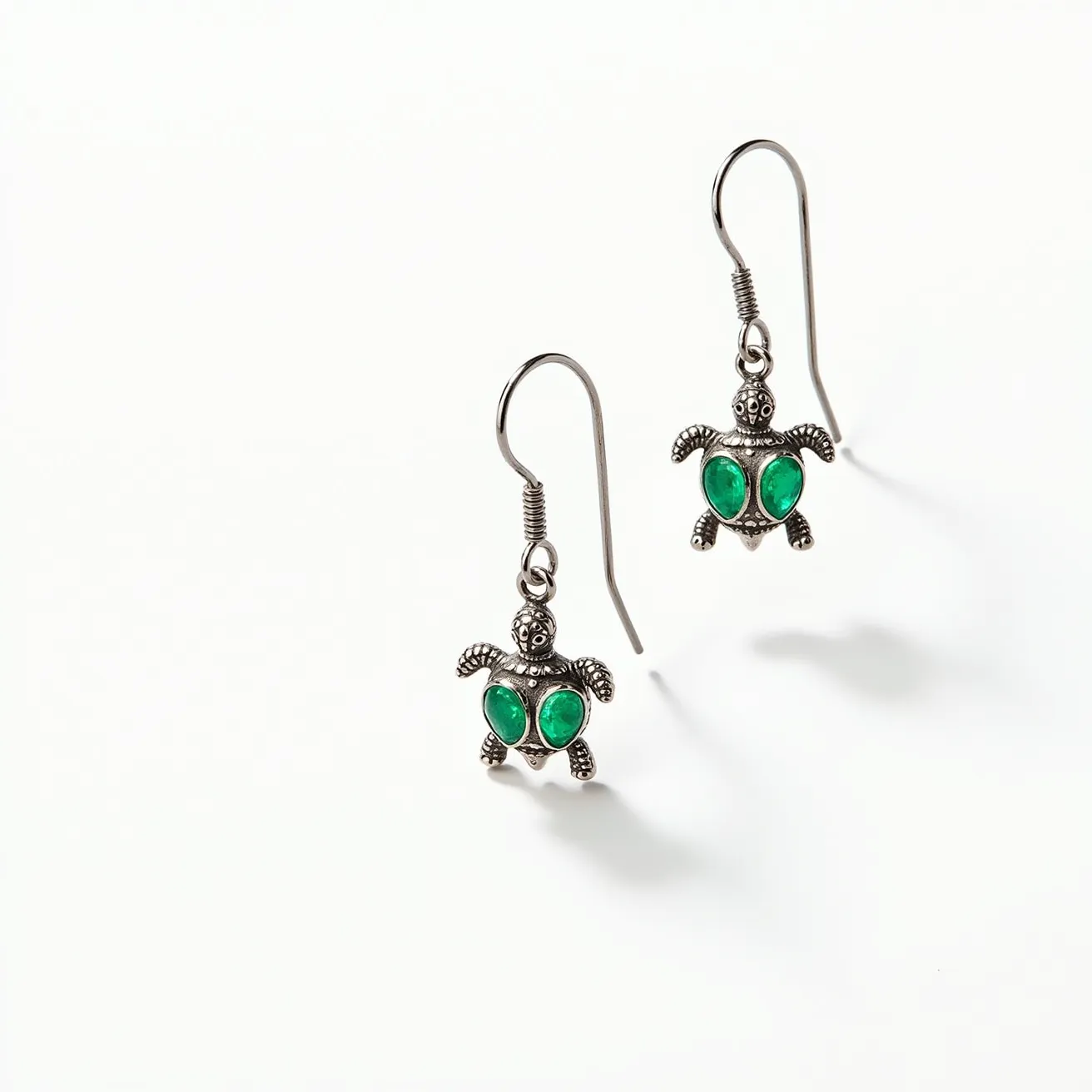 These turtle earrings are crafted from a metallic material, possibly silver or a silver-tone alloy, shaped into charming turtle designs. They feature green gem-like stones, set as the turtle's shell, with a smooth, cabochon cut, enhancing their vibrant color. The stones are secured in a bezel setting, providing a seamless integration with the metal frame. The earrings use a fish hook clasp for easy attachment, offering both functionality and elegance.