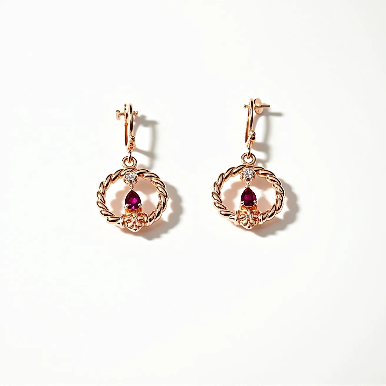 These twist earrings feature a beautifully crafted circular design in a gold-toned metal, creating an elegant braided effect. Within the circular frame, a pear-shaped red gemstone, likely a ruby, is set with a decorative gold element, adding a rich, colorful contrast. Above the red gemstone, a small round clear stone is set, potentially a diamond, providing an extra touch of sparkle. The stones are held securely in place with a prong setting. These earrings are attached with a lever-back clasp, ensuring both security and ease of wear.