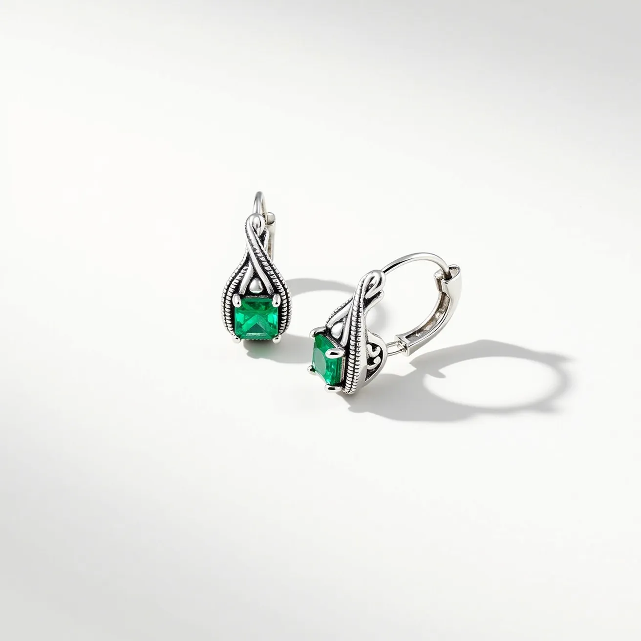 These twist earrings feature a refined design composed of silver-toned metal, creating an elegant twisted frame. They prominently display square-cut green gemstones, which are securely held in place by a bezel setting that complements the overall design. The earrings are designed with lever-back clasps, ensuring a secure and comfortable fit when worn.