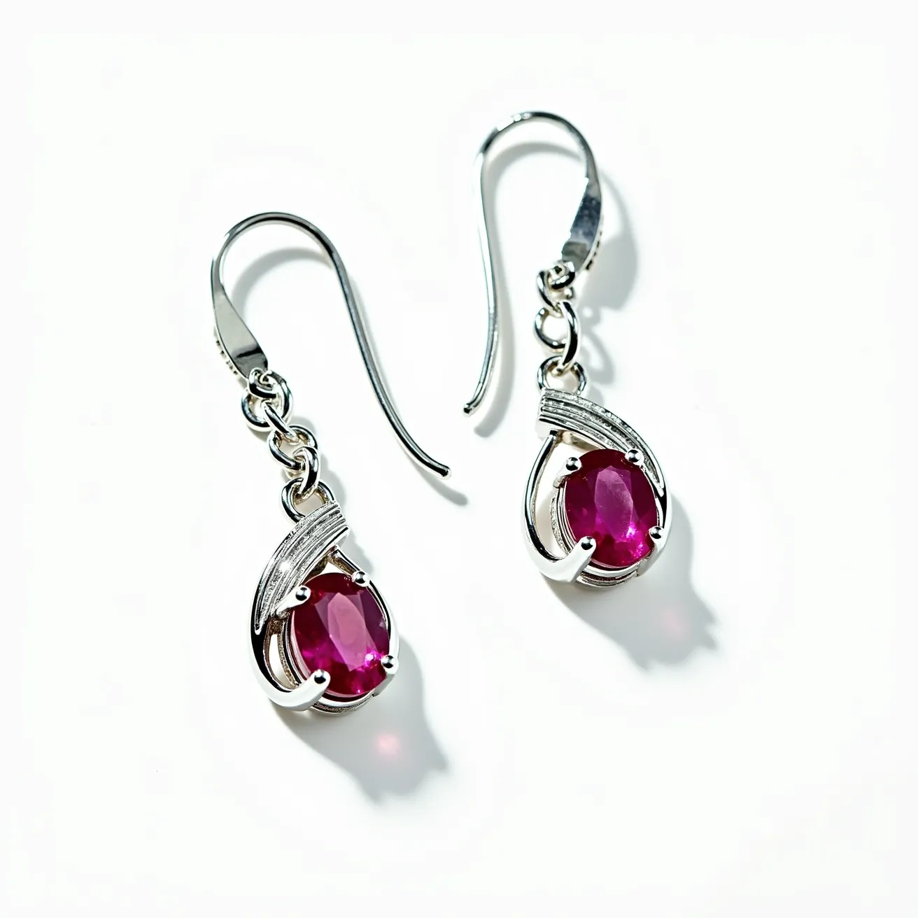 These twist earrings feature an elegant design crafted from a silver-colored metal, showcasing a sophisticated and polished look. The focal point of each earring is a vibrant oval-cut red gemstone, securely held in place by a classic prong setting that highlights its rich hue and sparkling facets. The twist design is accentuated by curved metalwork surrounding the gemstone, adding a dynamic and fluid aesthetic to the piece. The earrings are equipped with a simple fishhook attachment, allowing for easy wear and providing a graceful dangle when worn. The combination of the deep red stones with the sleek metal creates a striking contrast that enhances the earrings' overall allure.