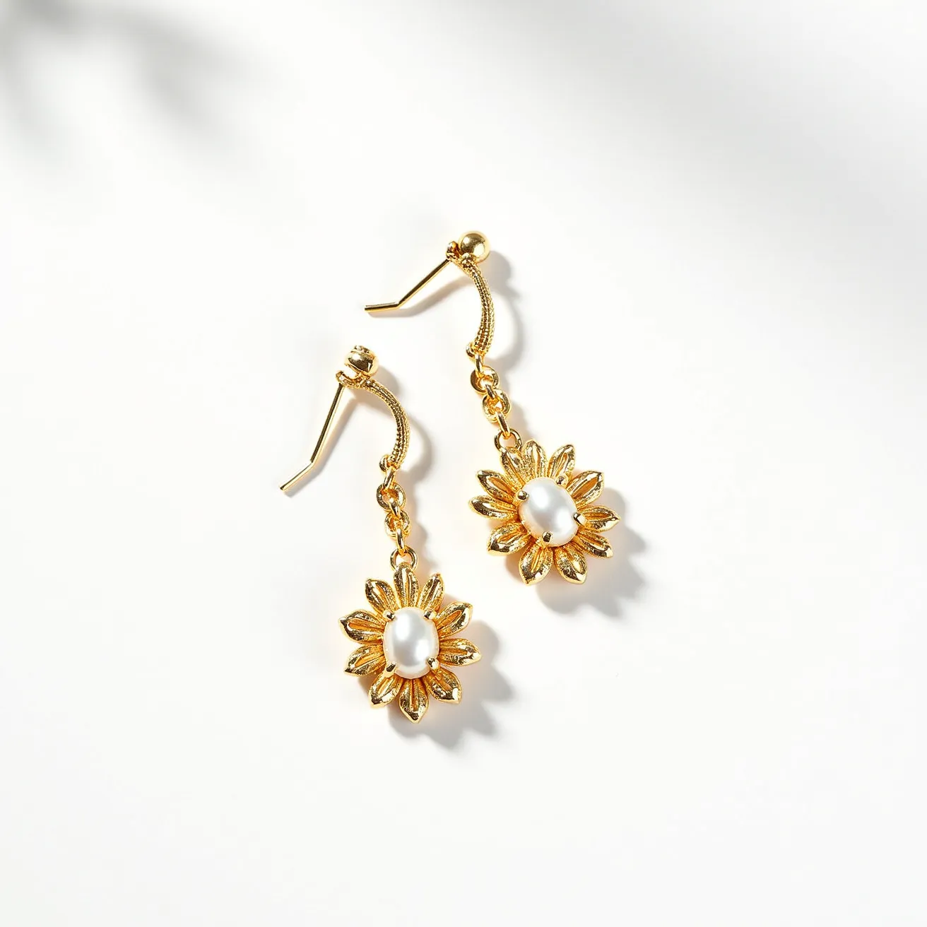 These twist earrings feature an elegant design with a gold-toned metal construction, showcasing a graceful flower motif. Each earring is centered with a smooth, oval pearl-like gem that adds a touch of sophistication, set in the middle of textured and polished petal shapes. The earrings are designed with a hook clasp, allowing for easy wear and secure attachment. The overall look is both delicate and striking, making these earrings a standout accessory for various occasions.