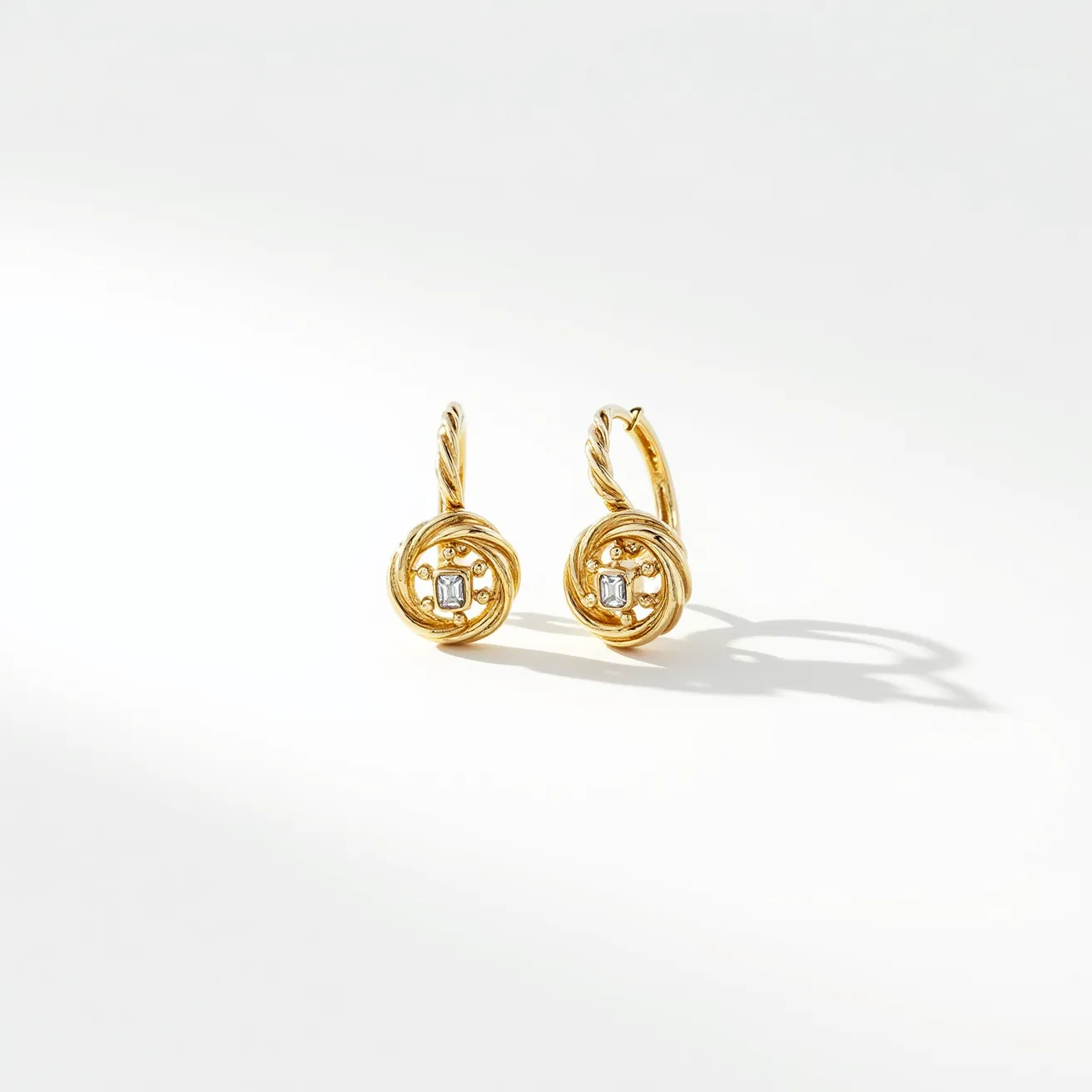 These twist earrings feature a unique design crafted from gold, evident in their warm, lustrous hue. At the center of each earring is a single rectangular-cut gemstone, likely a diamond, set within the intricate twisted patterns of gold that coil into a circular motif. These gemstones are securely held in a delicate prong setting, allowing light to enhance their brilliance. The earrings are equipped with a latch back clasp, ensuring both security and ease of wear. The elegant interplay of the twisted gold and the sparkling central gemstone creates a sophisticated and timeless aesthetic.