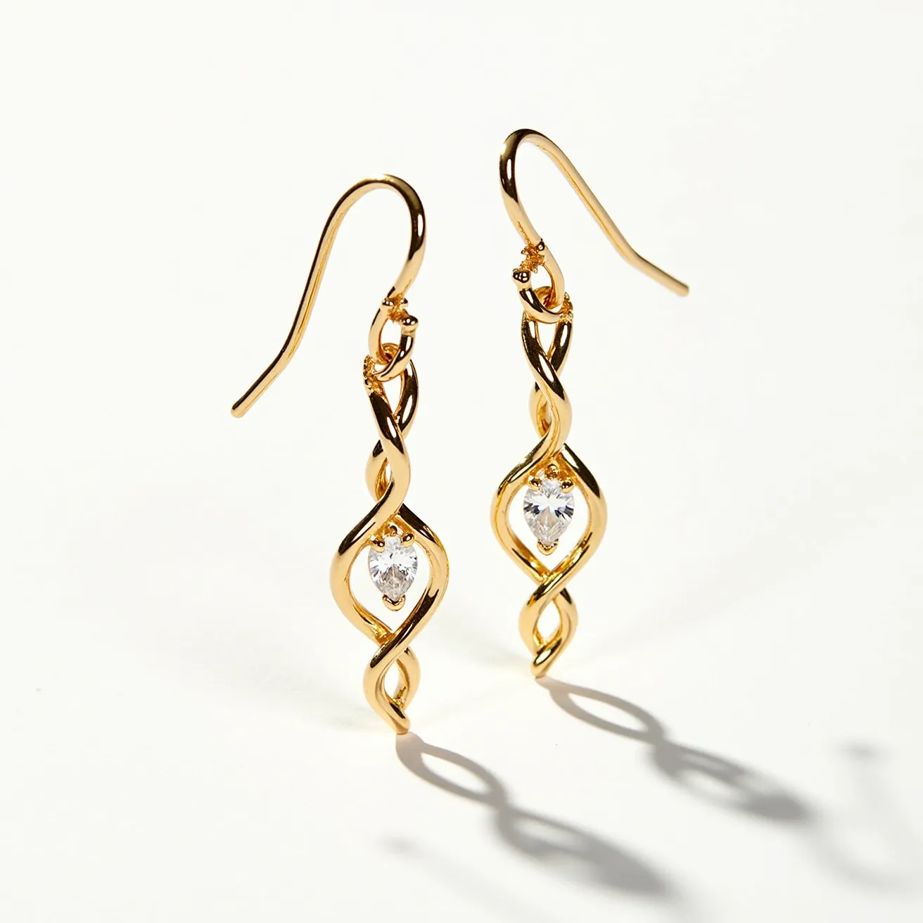 These twist earrings feature an elegant spiral design crafted from polished gold-tone metal, giving them a luxurious and sophisticated appearance. At the center of each earring, a pear-shaped clear stone is set securely, adding a sparkling focal point to the design. The stones are held in place by prongs that seamlessly blend with the metal, ensuring both security and style. The earrings are equipped with fish hook clasps, providing a comfortable and secure fit for pierced ears. The overall design combines fluid movement with a classic elegance, making these earrings a versatile accessory for various occasions.