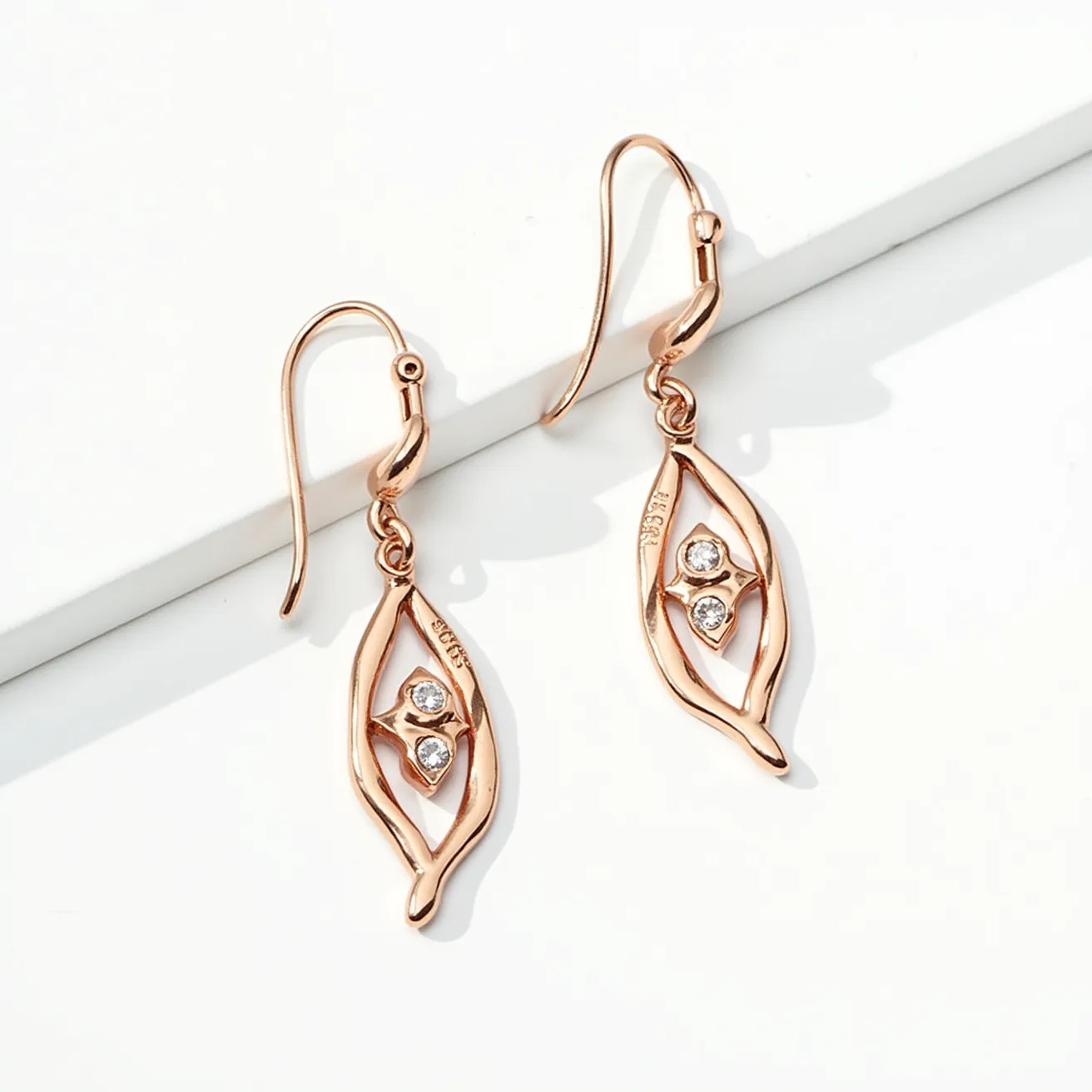 These twist earrings feature an elegant design crafted from a polished rose gold material. The central focus of the earrings is two round-cut stones, likely diamonds or diamond-like gems, set within the twisted frame, which enhance the earrings' refined look. The stones are bezel set, providing a secure and classic appearance. The earrings are designed with a hook attachment, offering ease of wear and a graceful dangle.