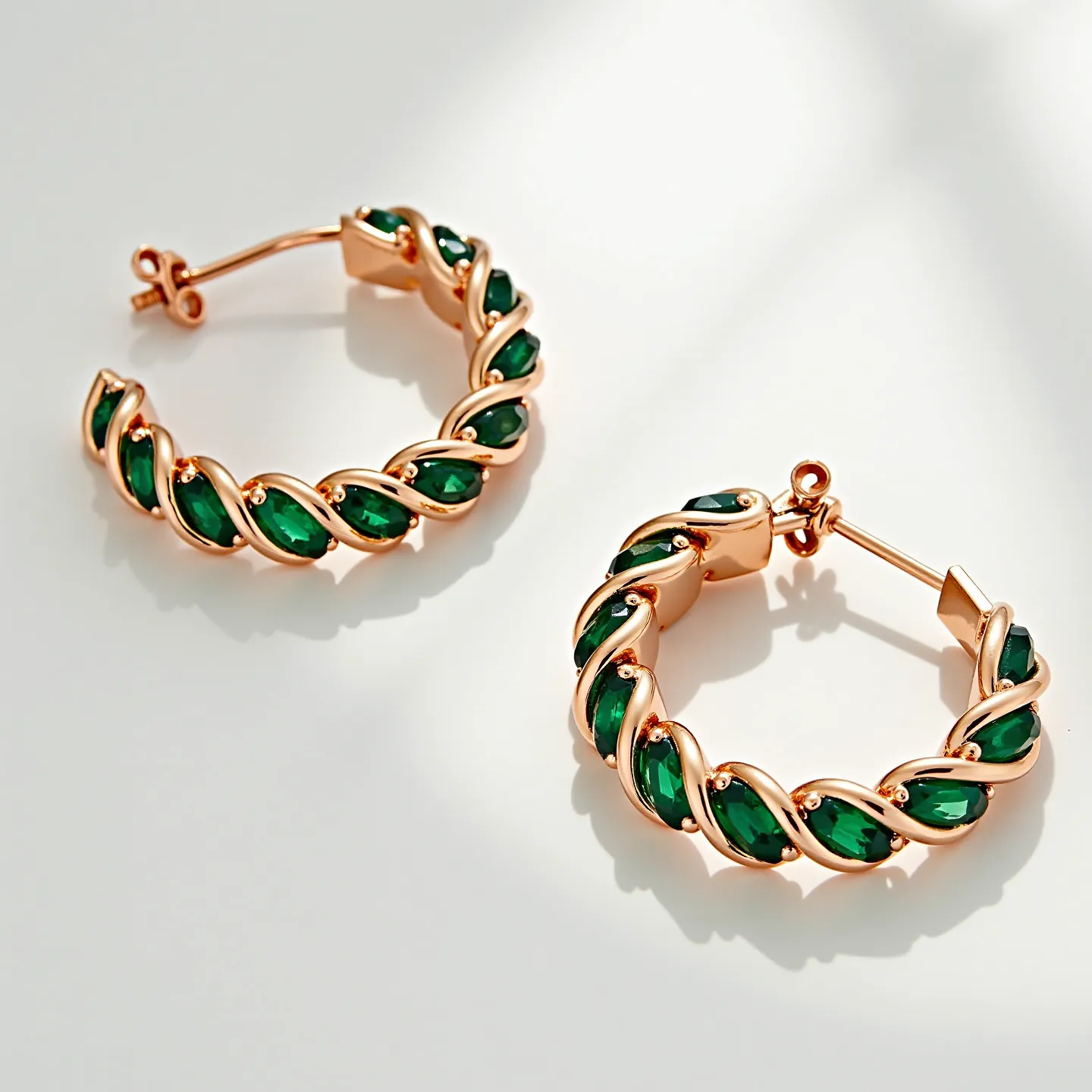 These twisted hoop earrings feature a captivating design with rose gold metal interlacing elegantly to create a spiral effect. The hoops are adorned with deep green marquise-cut gems, each securely set in a bezel-style that highlights their vibrant color. These earrings are equipped with a classic post and butterfly clasp, ensuring a secure fit while maintaining the graceful aesthetic. The combination of the twisted metallic design with the rich gems creates a sophisticated and eye-catching accessory.