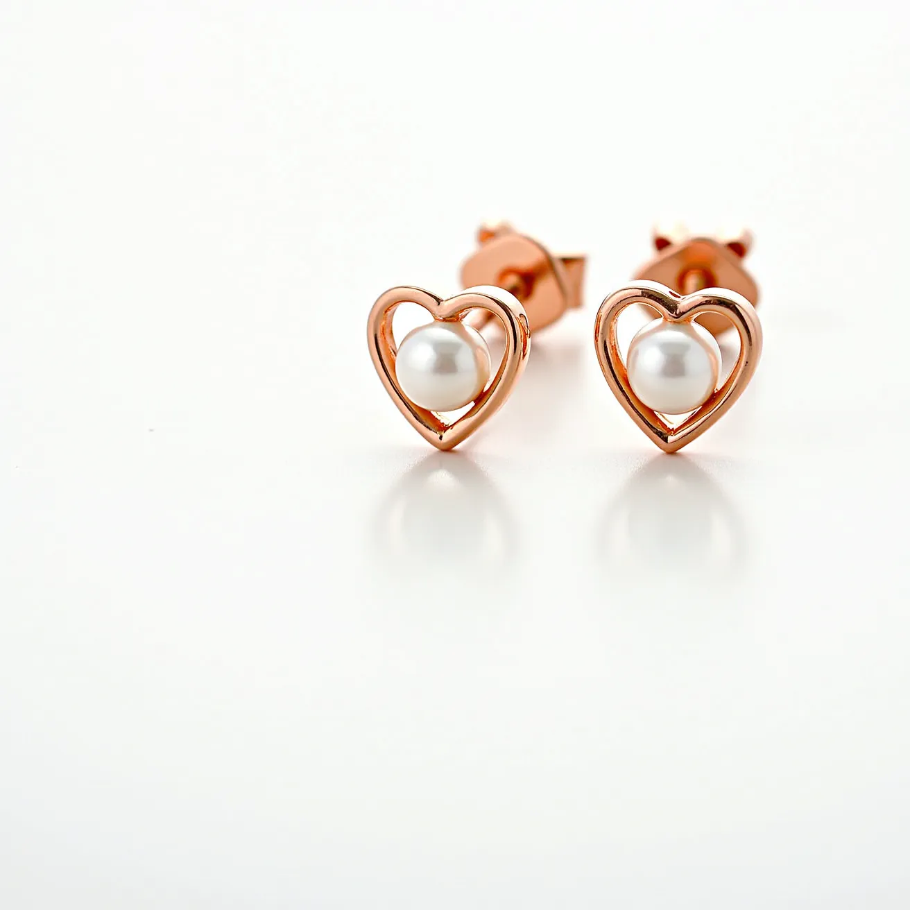 These valentines earrings feature a lovely heart-shaped design crafted from a warm rose gold metal. At the center of each heart sits a lustrous round pearl, adding an elegant touch to the earrings. The pearls are smoothly set, allowing them to be the focal point within the open-heart frame. These earrings are secured with a post and butterfly clasp attachment, ensuring they stay comfortably in place when worn. The combination of the rose gold and the classic pearls creates a romantic and timeless look.