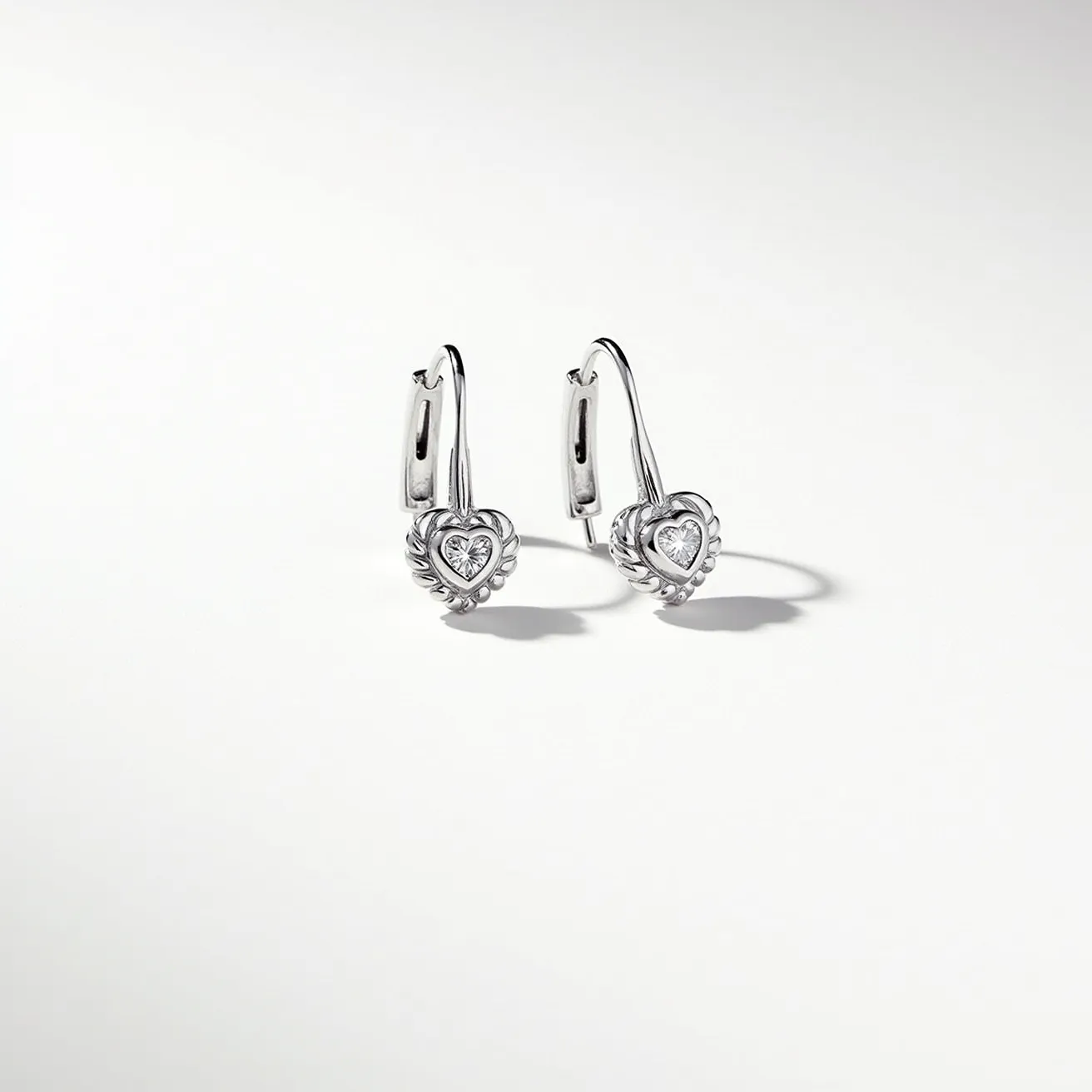 These Valentine's earrings feature a charming heart motif crafted from what appears to be polished silver, giving them a sleek and elegant appeal. The center of each heart holds a clear, round-cut gemstone set in a bezel setting, which adds a touch of sparkle and sophistication to the design. The earrings are attached with a lever-back clasp, providing both security and comfort for wear. The intricate detailing around the heart shapes further enhances their romantic theme, making these earrings a fitting accessory for any special occasion.