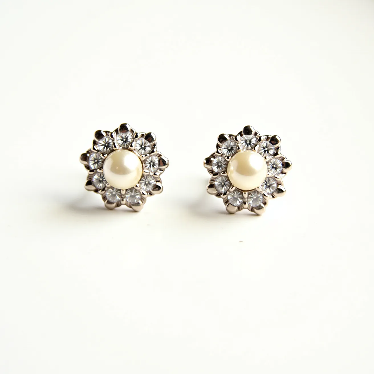 These valentines earrings feature a central pearl-like gem, set within a ring of clear, faceted stones that resemble small diamonds or cubic zirconia. Each stone is prong-set, creating a flower-like arrangement around the central gem. The earrings are designed as studs, meant to be secured with a post and back clasp, often used for ease of wear and security. The metal appears to have a shiny, silver-tone finish, complementing the lustrous quality of the central gem and the surrounding stones.