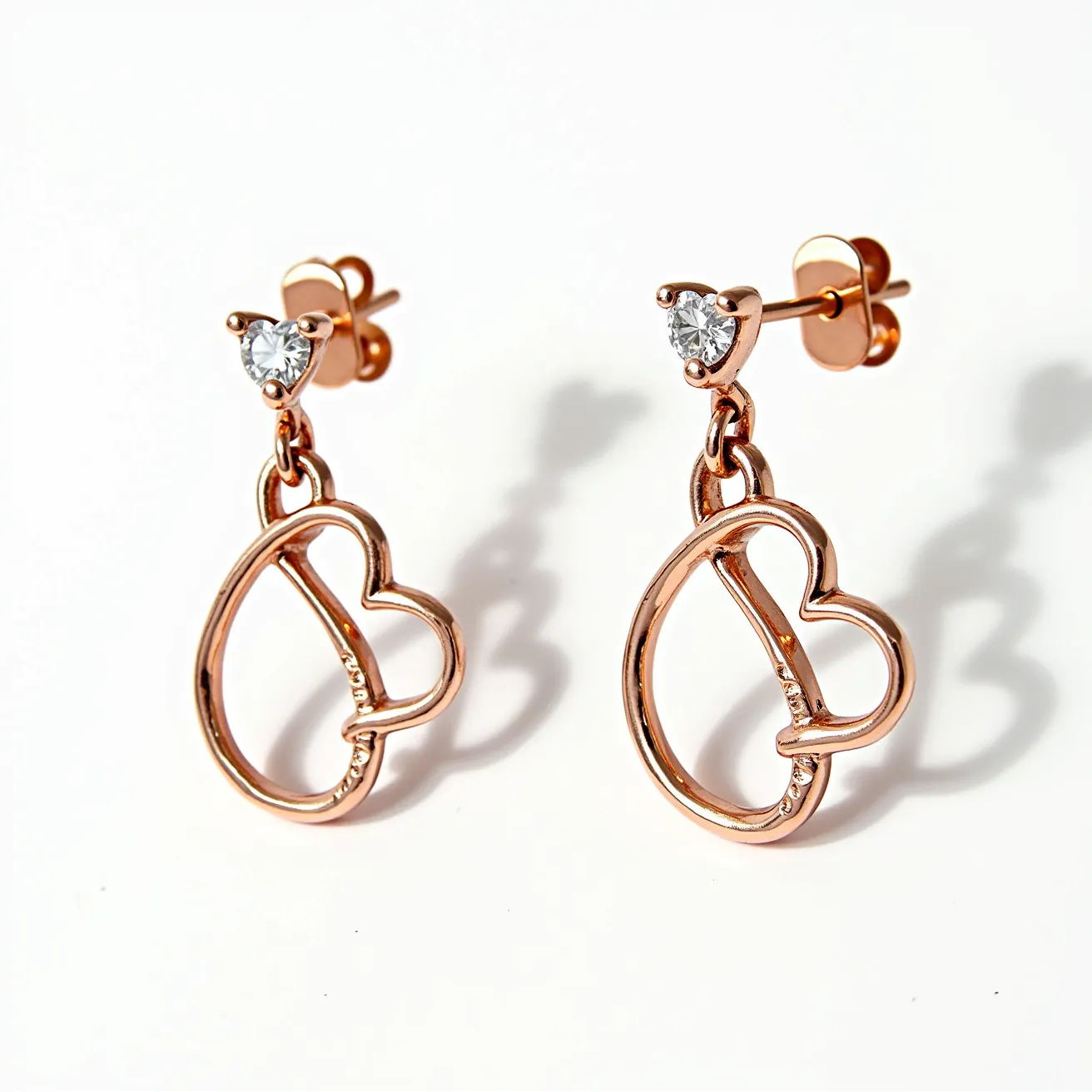 These valentines earrings are crafted from rose gold-toned metal, featuring an open-heart design that emphasizes elegance and romantic symbolism. Each earring is adorned with a single round-cut gem at the top, set in a three-prong setting that enhances its sparkle and brilliance. The earrings are secured with a post and butterfly clasp, providing both comfort and security for the wearer. The design showcases a harmonious blend of modern style and timeless romantic motifs, making them an ideal accessory for expressing affection.