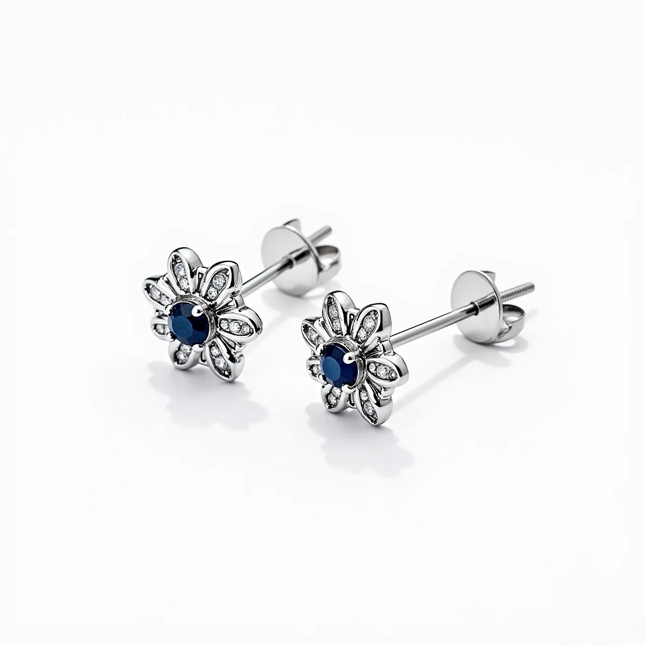 These white earrings feature a delicate floral design with a central dark blue gemstone, likely a sapphire, cut in a round shape. Surrounding the central stone are smaller clear stones, possibly diamonds or cubic zirconia, set in petal-shaped metal casings that enhance the overall floral motif. The earrings appear to be crafted from a shiny metal, possibly silver or white gold, contributing to their elegant aesthetic. They are secured with screw-back posts, ensuring a snug and secure fit when worn.