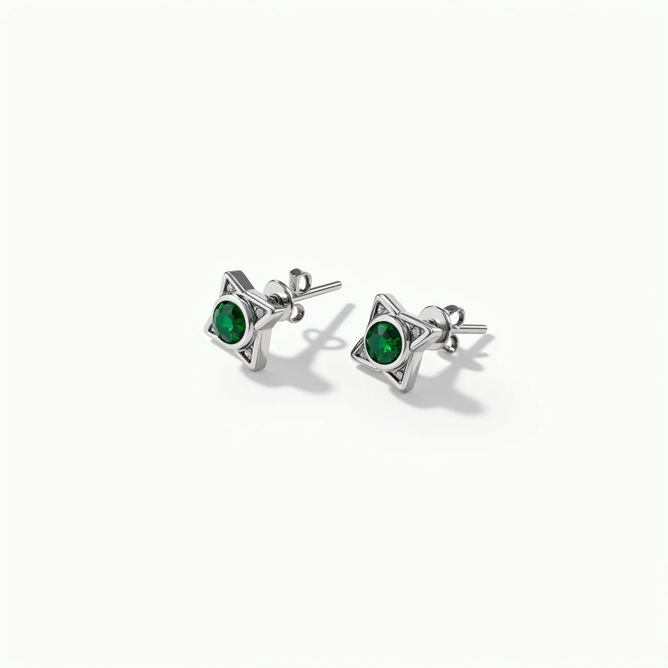 These white earrings feature a modern geometric design incorporating a star shape. At the center of each earring is a vivid green gemstone, likely an emerald, cut into a round shape and set securely within the star motif. The metal appears to be a polished silver, offering a sleek and contemporary look. The earrings are designed with a post-back closure, ensuring a secure and comfortable fit for the wearer. The aesthetic is both elegant and playful, making them a versatile accessory.