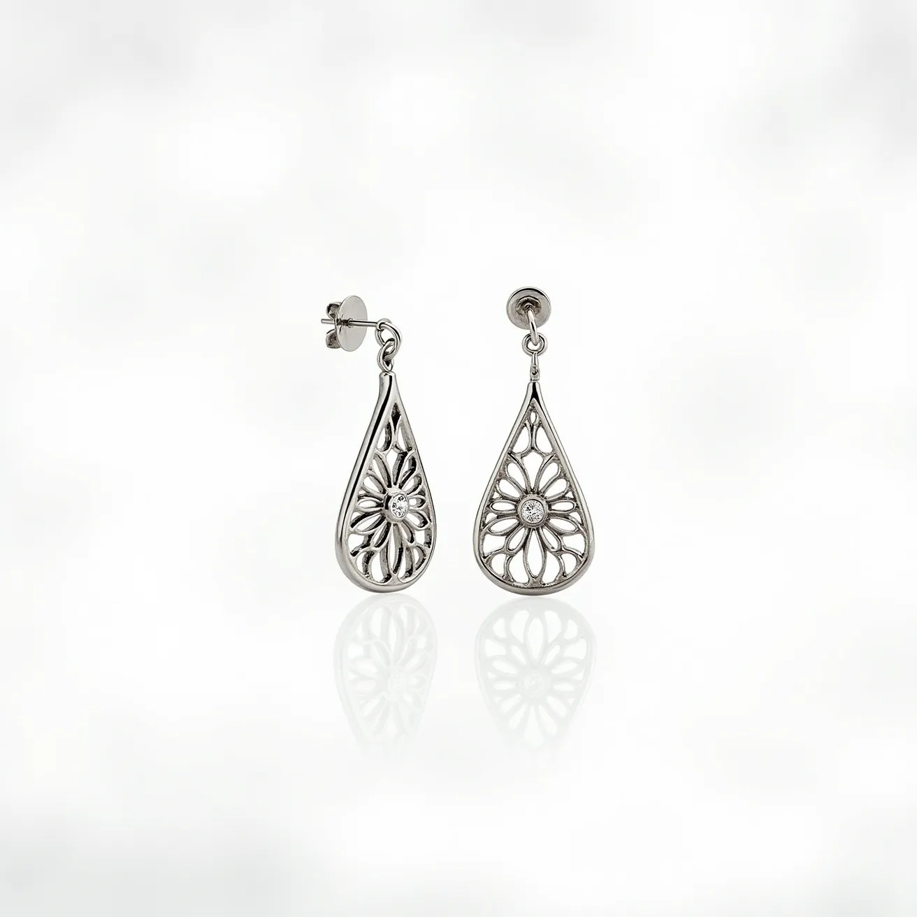 These white gold earrings feature a teardrop shape with an intricate floral design, each housing a small, centrally set round-cut diamond. The latticework in the design allows for an elegant display of craftsmanship, highlighting the brilliance of the metal and stone combination. The earrings utilize a stud backing for secure attachment, ensuring they remain comfortably in place while worn.