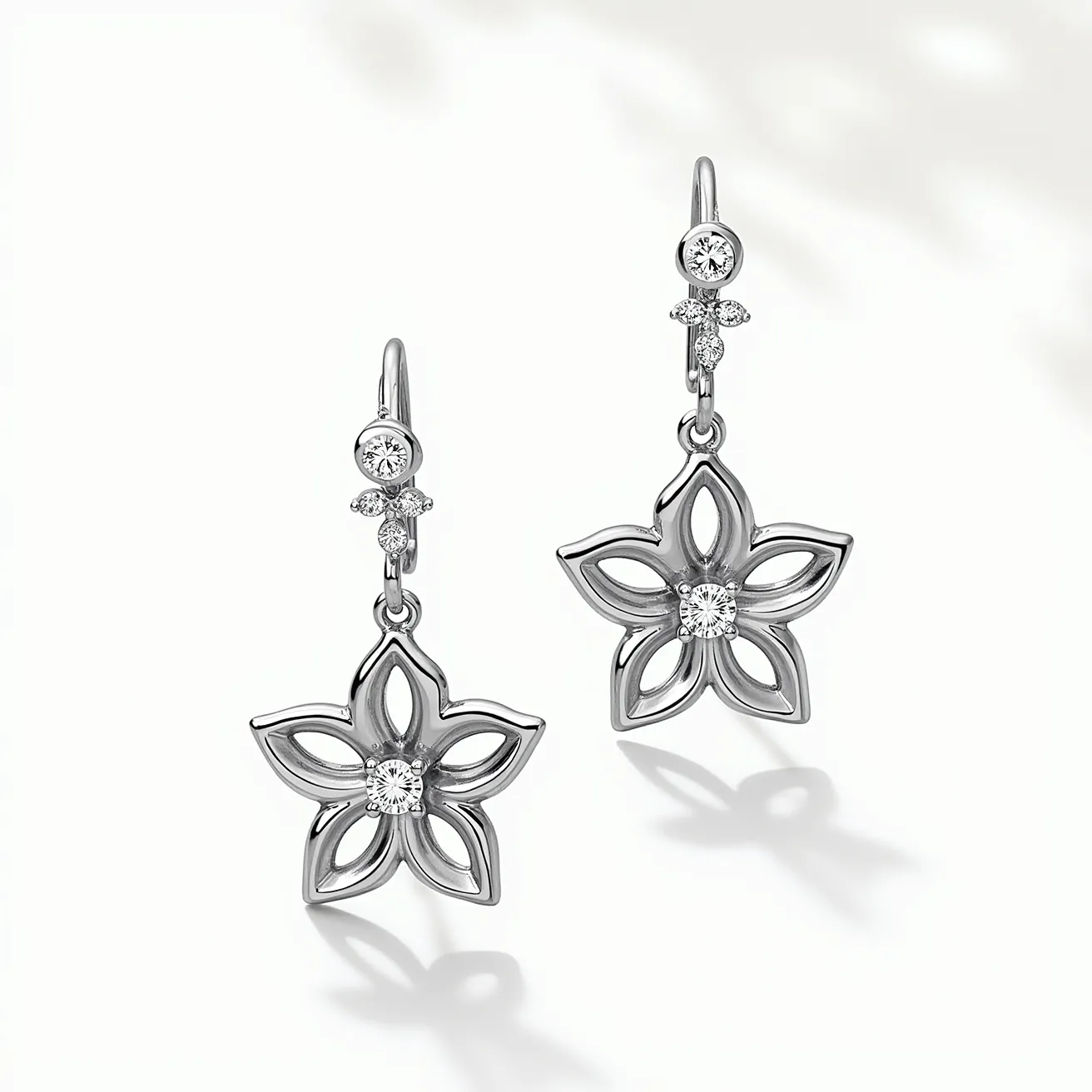 These white sapphire earrings feature a delicate floral motif, crafted with a metal that appears to be white gold or platinum. Each earring showcases a central round-cut white sapphire set securely in the middle of the flower design, enhancing its sparkling allure. Surrounding the centerpiece are intricately crafted petals, adding a touch of elegance and sophistication. Above the floral design, a small, bezel-set white sapphire connects the pendant to the earring hook, which is simple yet sturdy, ensuring a secure attachment when worn. The overall design is refined and graceful, making these earrings a charming accessory.