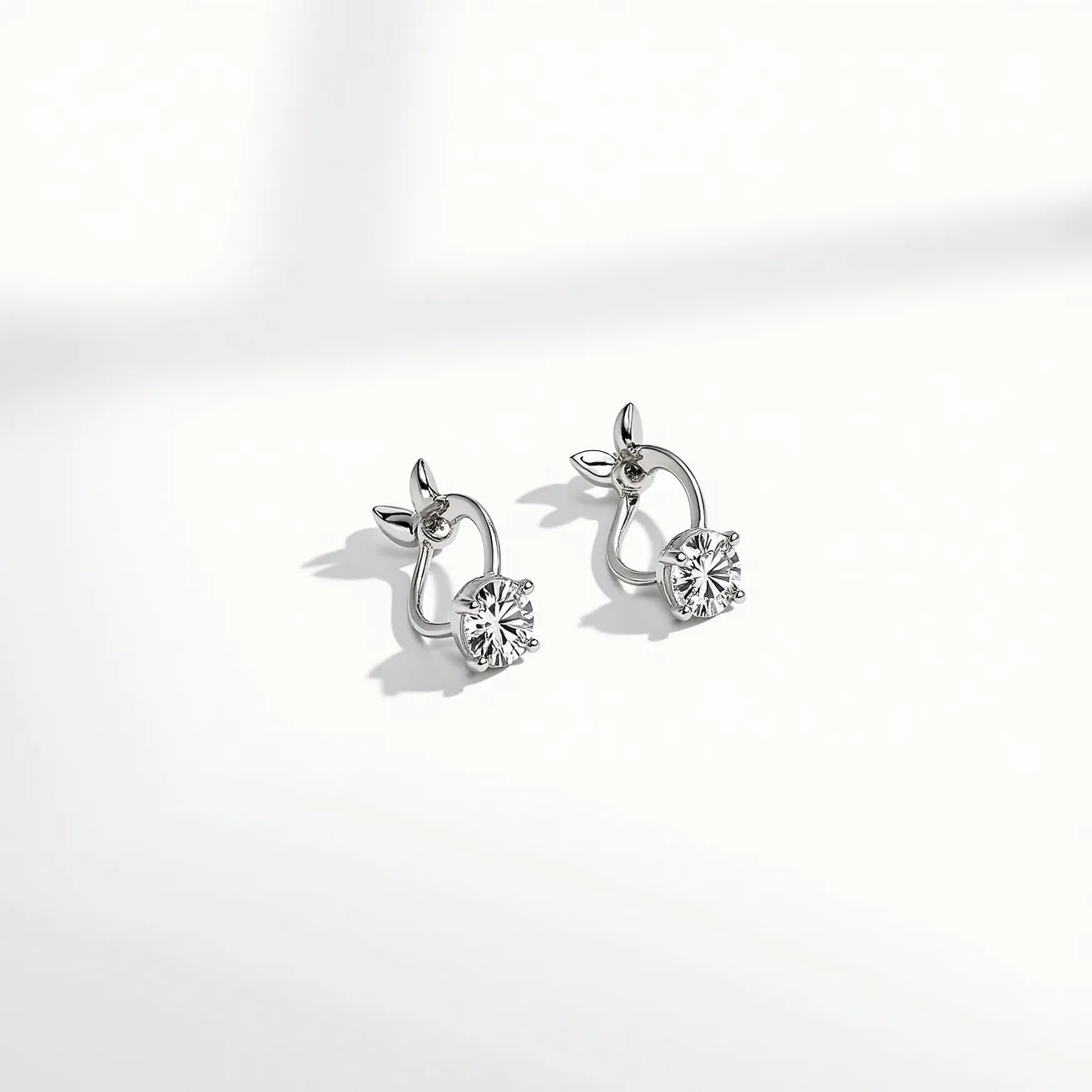 These white sapphire earrings feature round-cut white sapphires set in a four-prong setting, exuding a classic and elegant style. The sapphires are carefully mounted in a high-polish metal, likely silver or white gold, enhancing their brilliance and clarity. The design is completed with a unique floral-like accent at the top of each earring, adding a touch of whimsy and sophistication. They appear to have a secure hoop clasp, ensuring both style and practicality. The overall aesthetic is timeless, making these earrings suitable for both casual and formal occasions.