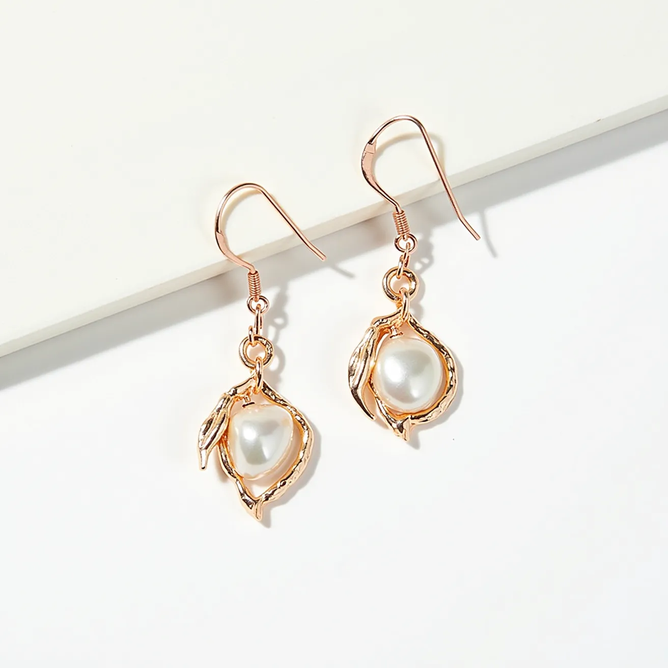 These wire earrings feature a delicate design composed of a lustrous white pearl set in a gold-toned wire frame, which wraps gracefully around the gem resembling a leaf design. The pearls are prominently displayed at the center of each earring, adding elegance and sophistication. The earrings use a simple hook clasp for easy attachment to the ears, complementing the overall delicate aesthetic of the piece. The combination of the wire frame and the pearl creates a harmonious blend of textures and colors, making these earrings suitable for both casual and formal occasions.