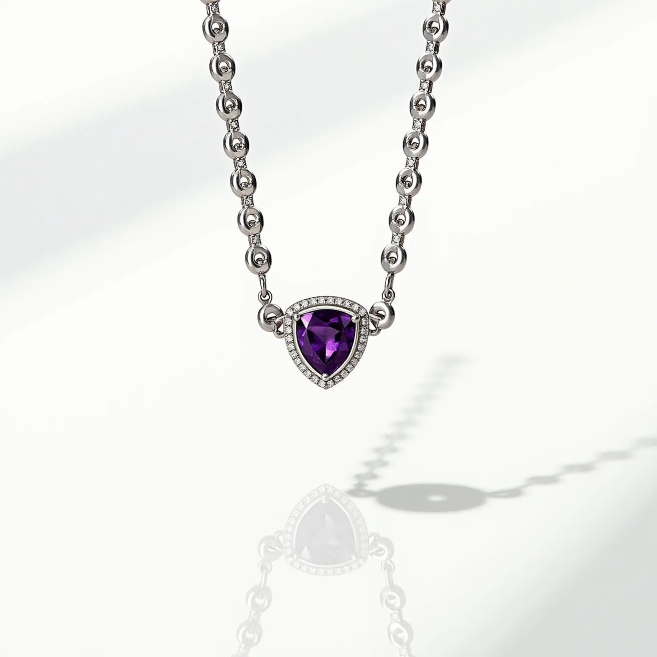 This alexandrite necklace features a striking deep purple stone, likely an alexandrite, cut in a unique trillion shape. The stone is set in a bezel adorned with small, sparkling round diamonds that enhance its brilliance. The pendant is attached to a chain composed of alternating small and larger round links, likely crafted from a white metal such as silver or white gold, which complements the setting. The overall design is elegant and modern, combining the sophistication of the gemstones with the sleekness of the metallic elements.