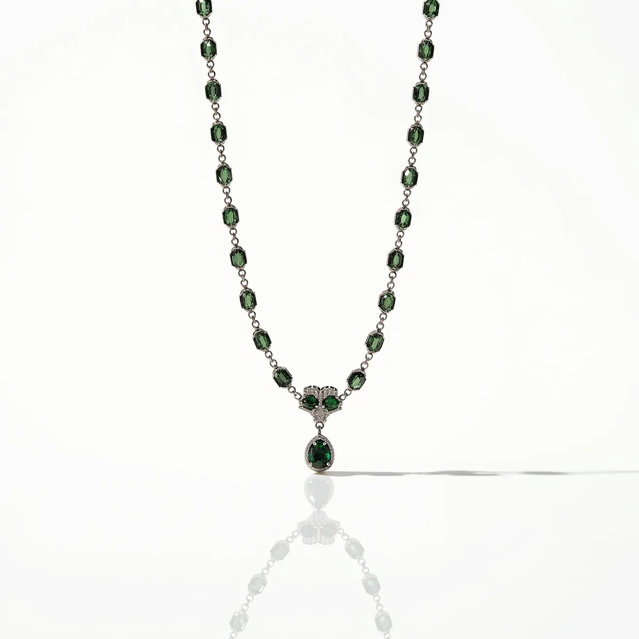 This alexandrite necklace features a delicate chain adorned with multiple green emerald-cut alexandrite gemstones set in a uniform, symmetrical pattern. Each stone is mounted in a classic prong setting, providing both elegance and security. The centerpiece of the necklace showcases a finely crafted, teardrop-shaped alexandrite, enhancing its visual allure. The stones are interconnected by links that likely consist of a precious metal, ensuring durability and a cohesive design. A secure clasp is present to fasten the necklace comfortably around the neck.