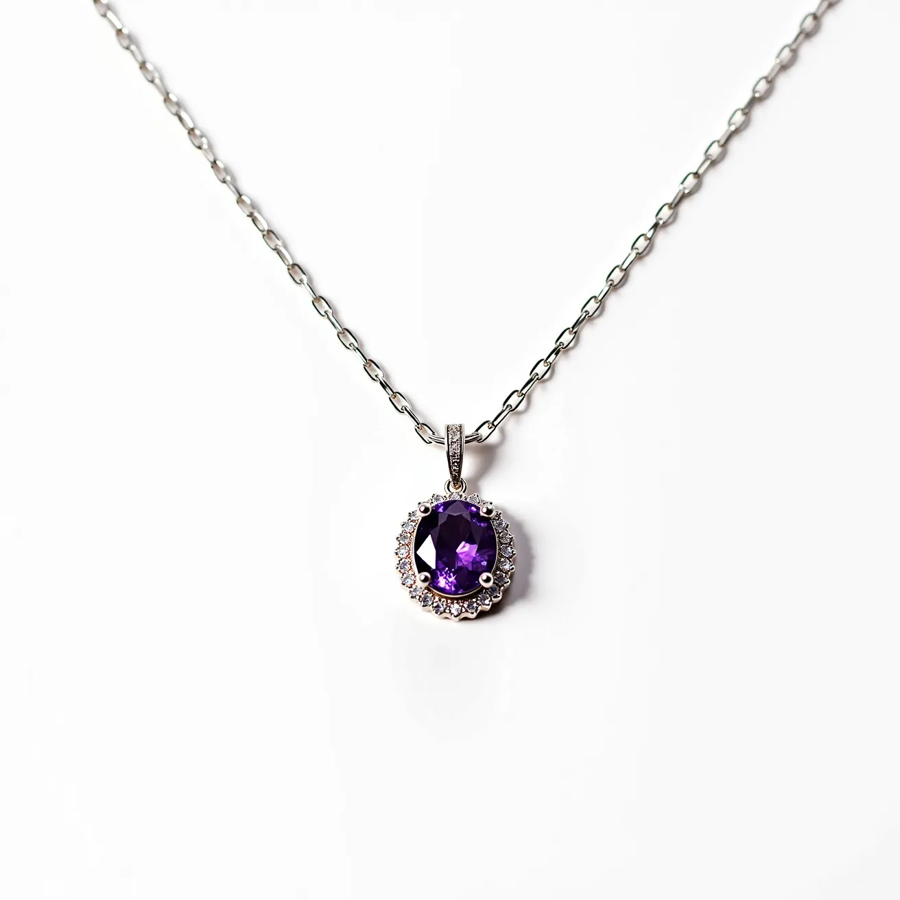 This alexandrite necklace features a stunning oval-cut alexandrite gemstone at its center, known for its captivating color-changing properties. The gem is elegantly surrounded by a halo of small, sparkling diamonds set in a prong setting, enhancing its brilliance and providing a classic, sophisticated look. The pendant is attached to a delicate silver chain, which complements the overall elegance of the necklace. The chain is likely secured with a standard lobster clasp, ensuring both style and security for the wearer.