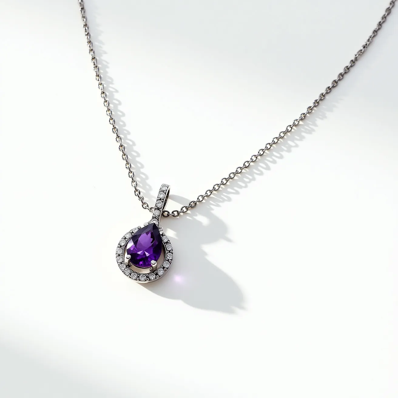 This alexandrite necklace features a central, pear-shaped, faceted gemstone, possibly alexandrite, noted for its deep purple hue. The gemstone is elegantly set in a halo setting, surrounded by a series of small, round brilliant-cut diamonds, adding sparkle and enhancing the overall allure of the pendant. The pendant hangs from a delicate chain, likely crafted from white gold or platinum, which complements the cool tones of the stones it supports. The necklace is secured with a simple yet sturdy clasp, ensuring ease of wear and security for the intricately designed piece.