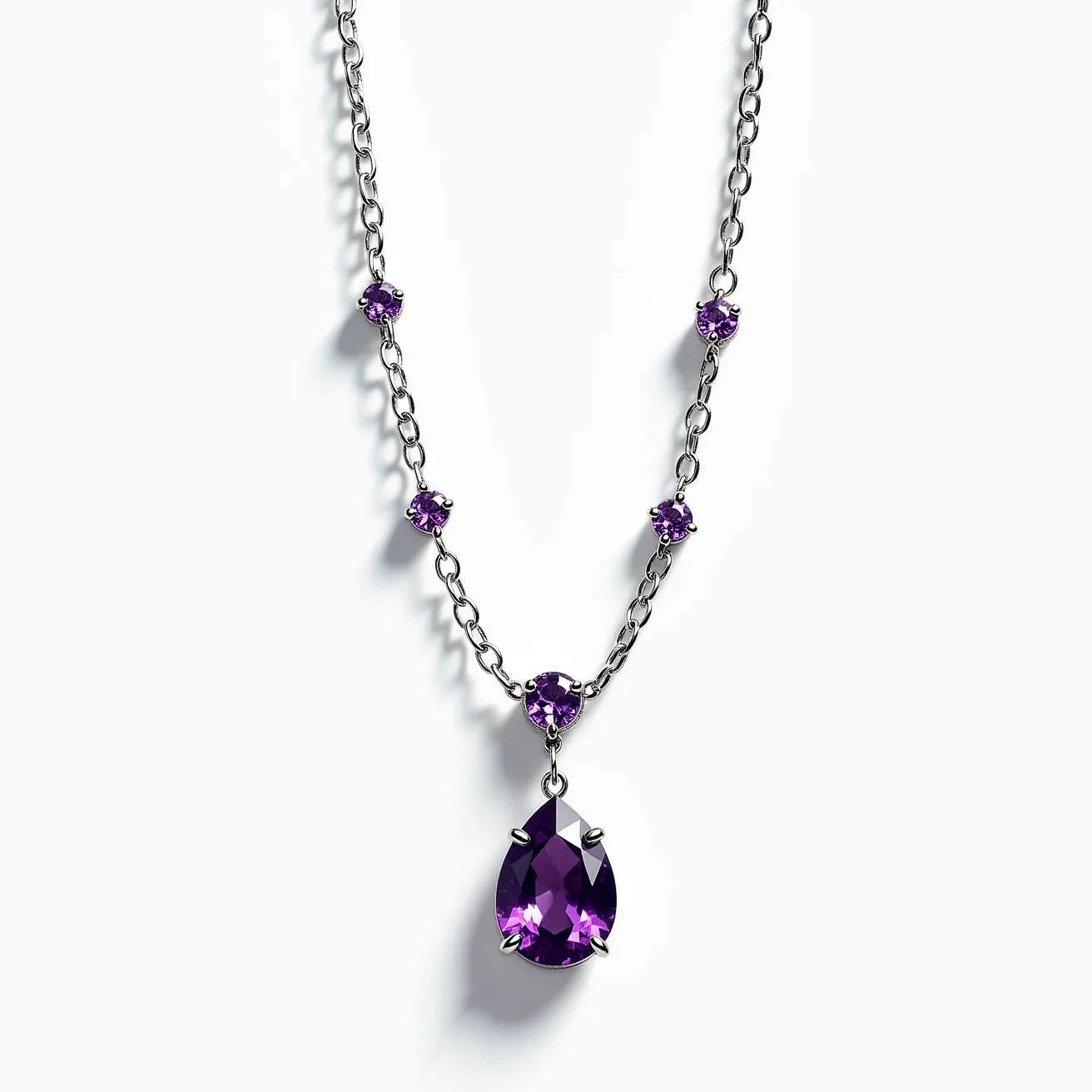 This alexandrite necklace features a delicate chain crafted from a silvery metal, likely white gold or platinum. The necklace is adorned with multiple round-cut alexandrite stones set along the chain, each secured in a simple, elegant prong setting that highlights their color-changing attributes. The centerpiece of the necklace is a larger, teardrop-shaped alexandrite pendant, also set in a prong setting, which draws attention to its unique brilliance and color play. The overall design combines simplicity and sophistication, allowing the unique qualities of the alexandrite stones to stand out.