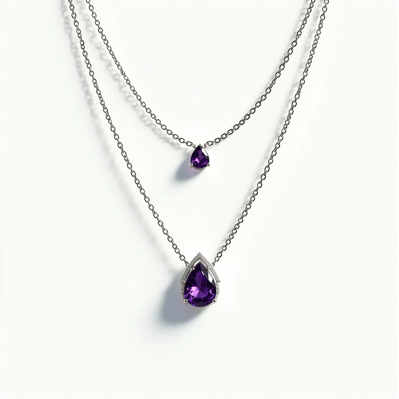 This alexandrite necklace features two tiers of delicate chain, showcasing pear-shaped stones prominently. The upper pendant is a smaller pear-cut gem, securely held by a simple prong setting. The lower pendant is a larger pear-shaped cut, surrounded by a refined halo setting that adds sophistication to the piece. These stones exhibit a rich purple hue, typical of high-quality alexandrite under certain lighting conditions. The necklace likely uses a standard clasp attachment, designed to blend seamlessly with the elegance of the design. The craftsmanship emphasizes both simplicity and luxury, making it a captivating accessory.